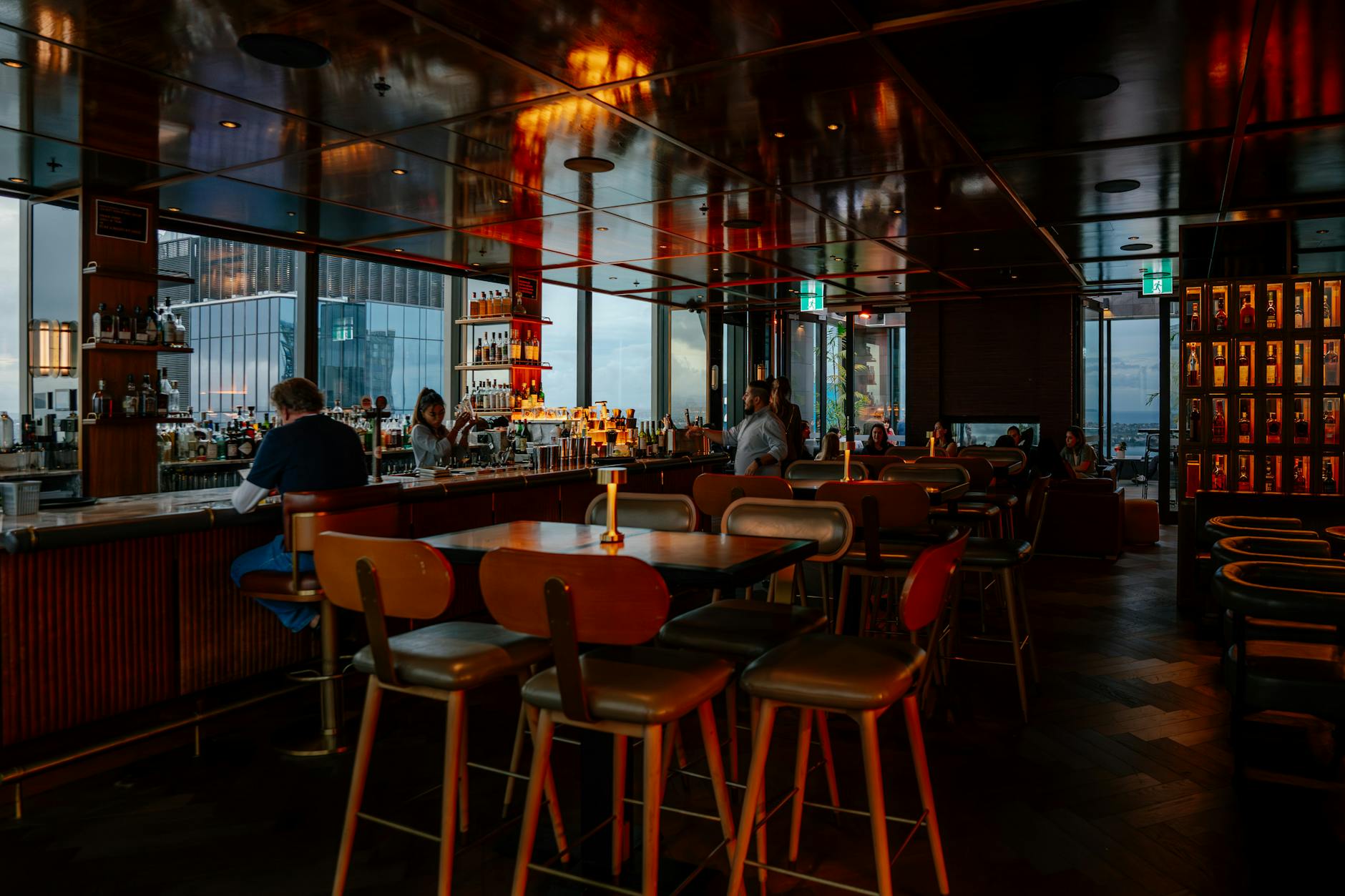 Warm dimly lit interior of a rooftop bar with patrons enjoying drinks and city skyline