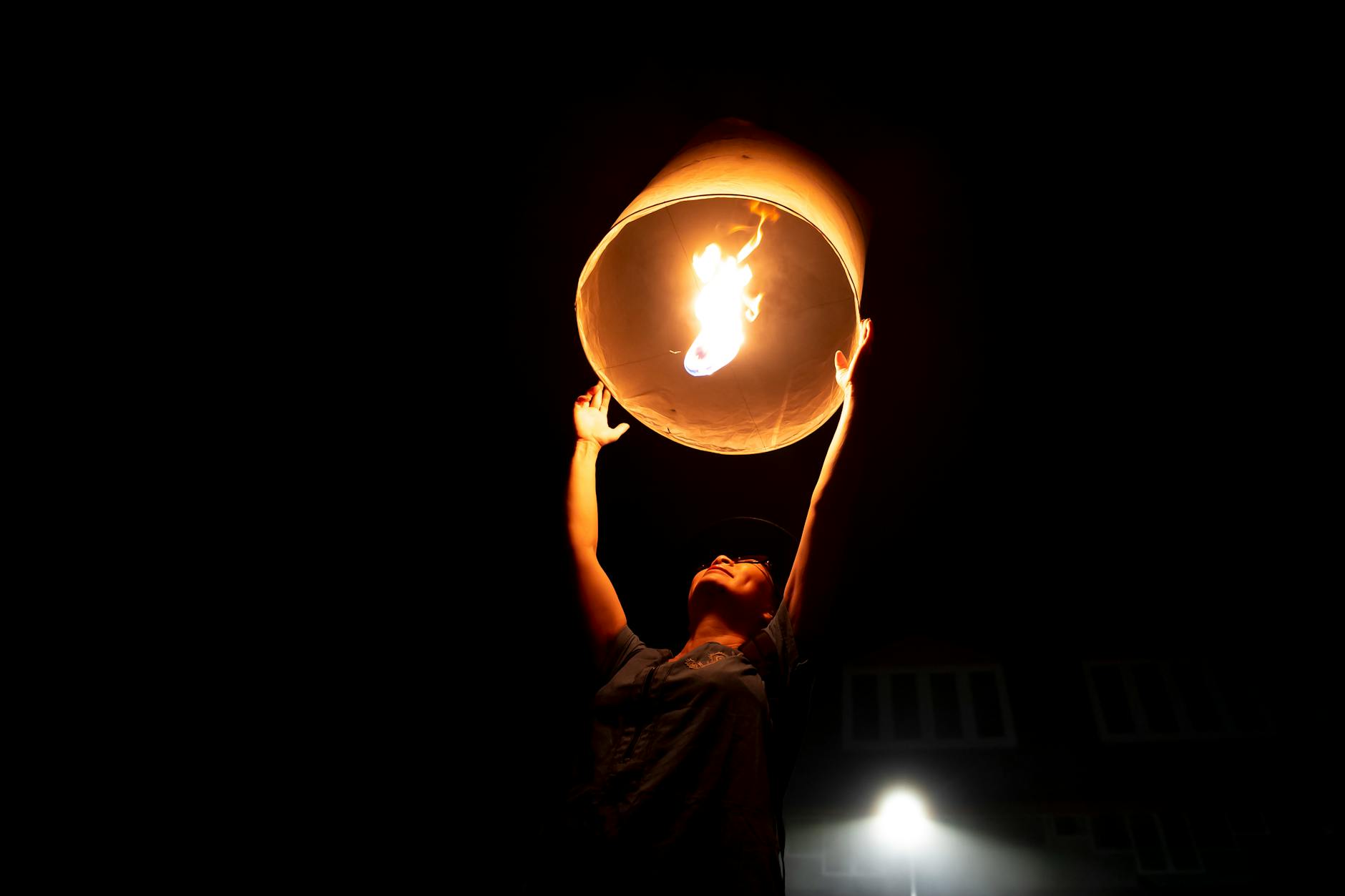A person launching an illuminated sky lantern against a dark night sky