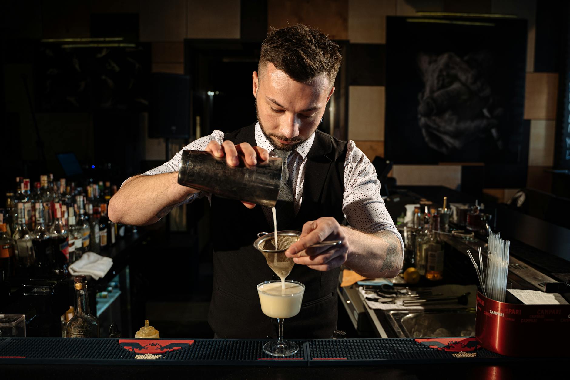 Bartender pouring a cocktail through a strainer in a stylish lounge bar