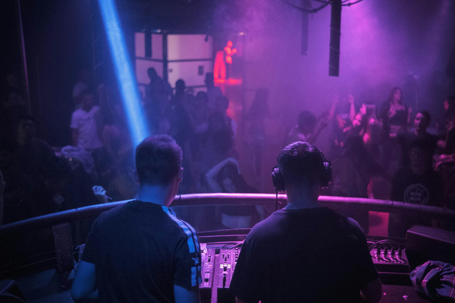 DJ mixing music at a lively nightclub with vibrant lights and dancing crowd