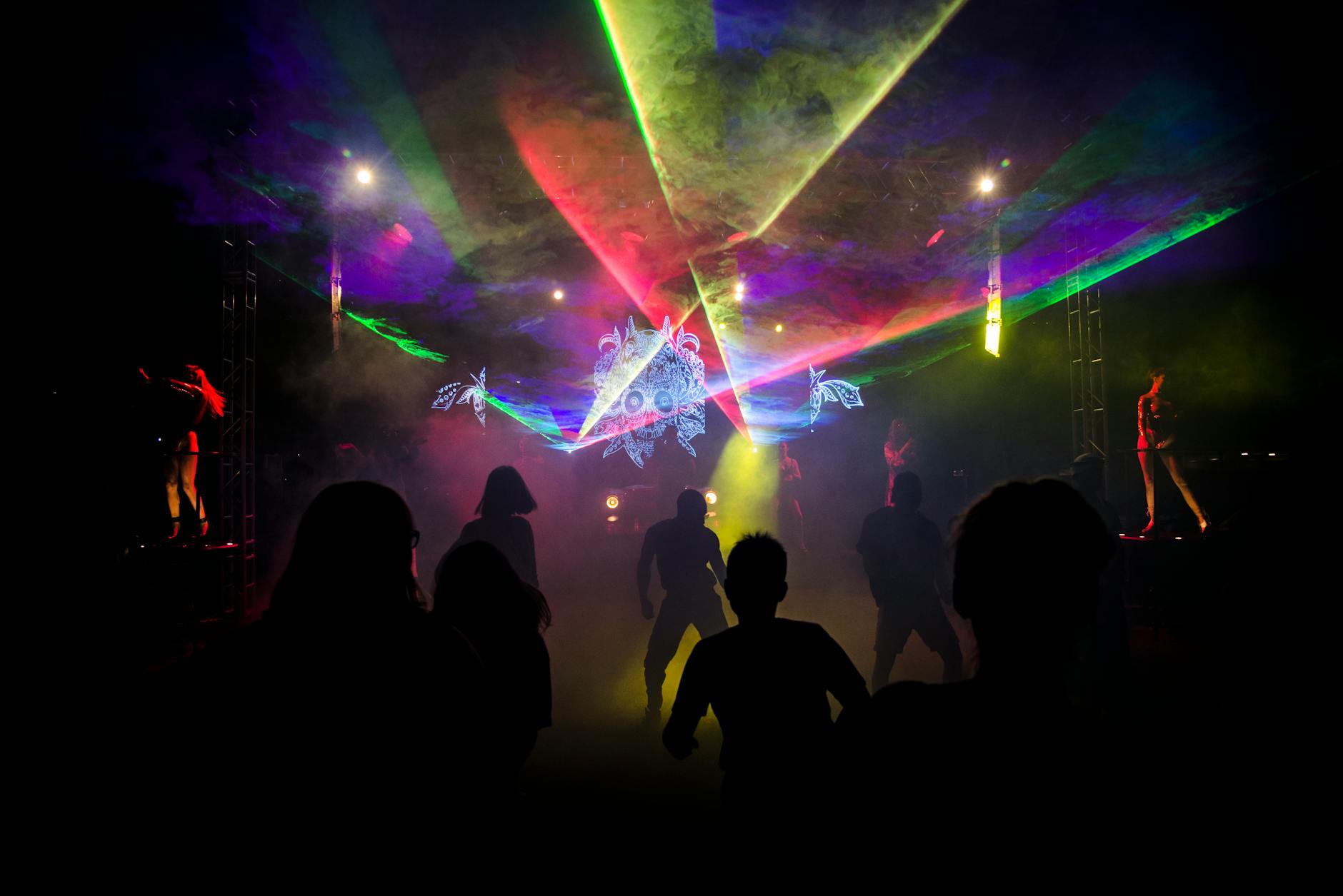 Silhouettes dancing under colorful laser lights in a vibrant nightclub setting