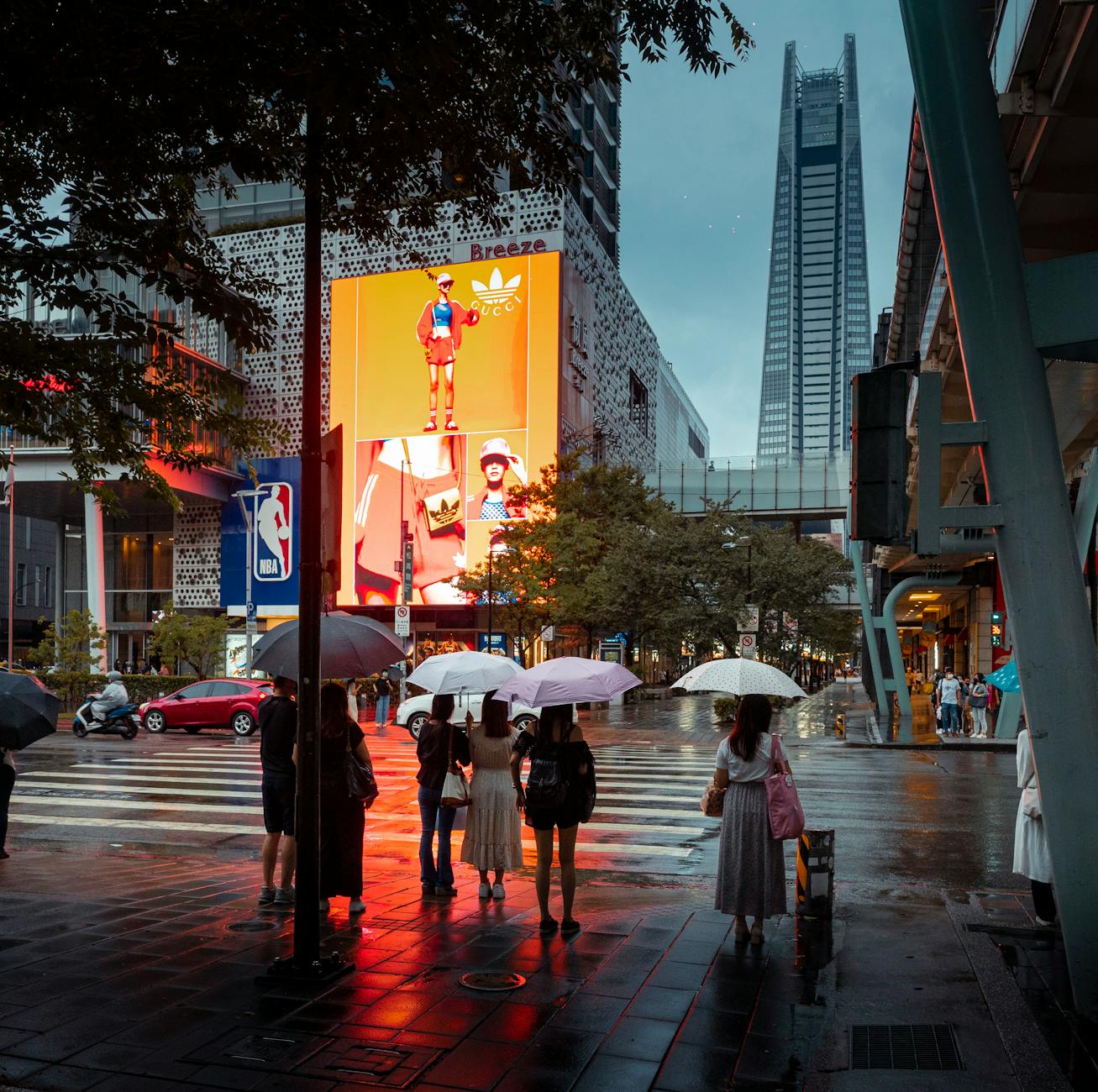 People walking on a wet city street at dusk with illuminated lights