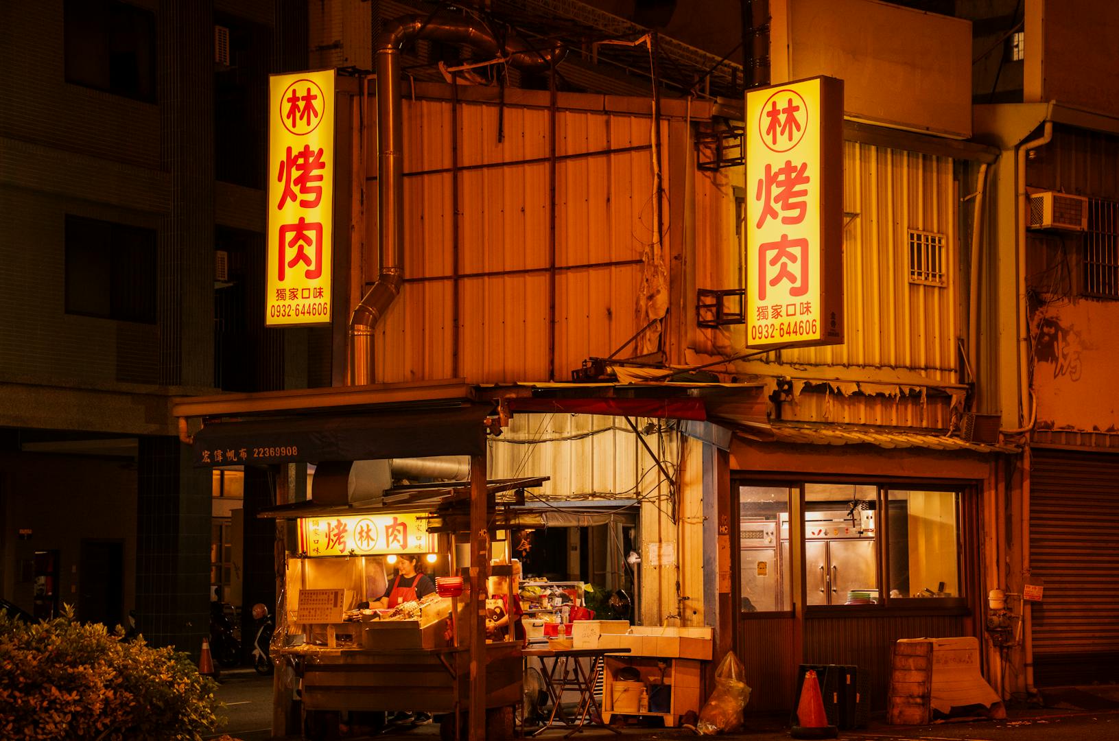 Late-night Taipei street with illuminated 24-hour eatery and customers