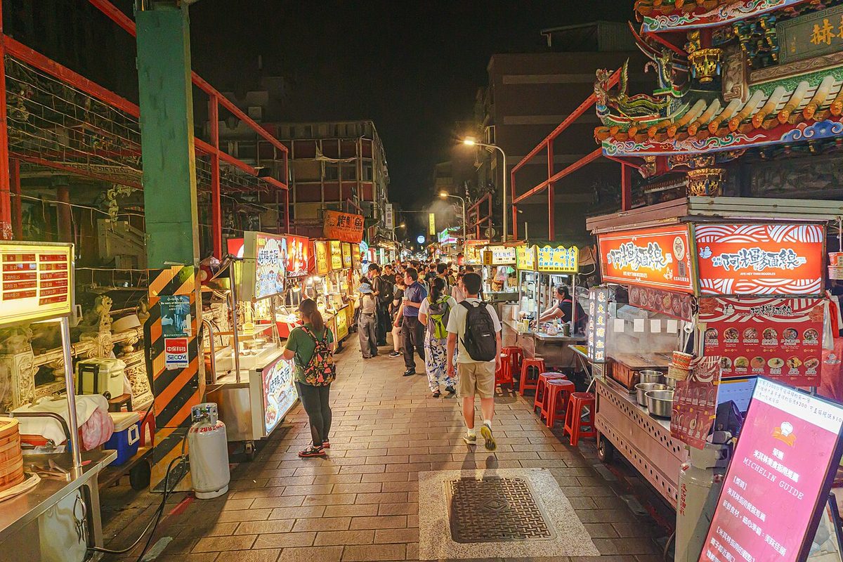 A vendor cooking night market food at a busy Taipei night market stall in the evening