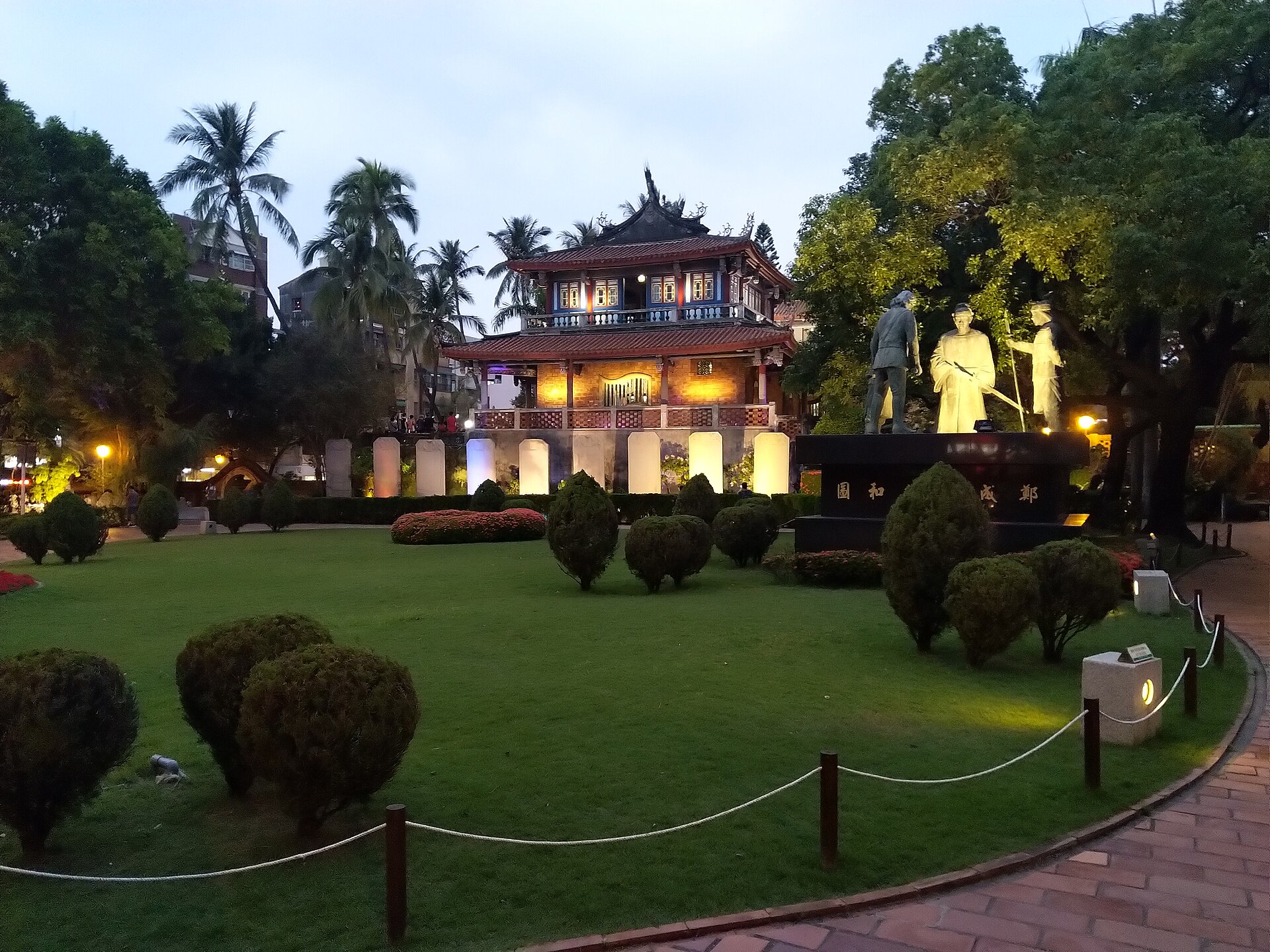 Chihkan Tower in Tainan lit at dusk with palm trees and a statue group in the garden