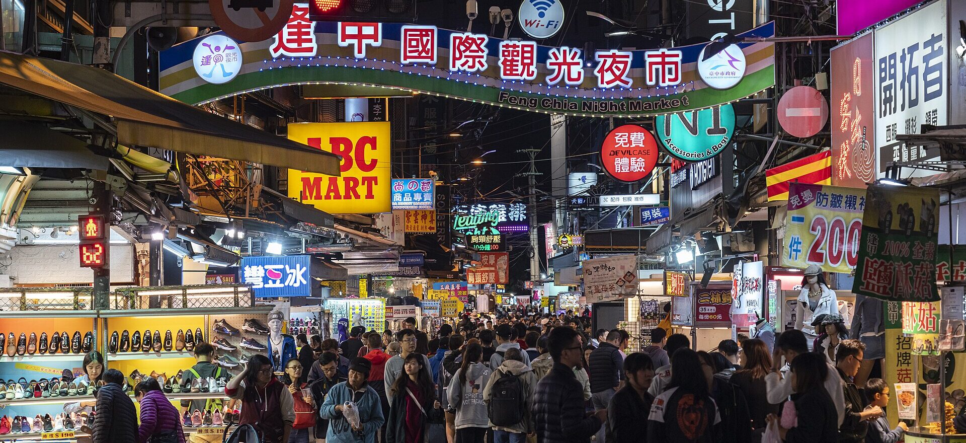 Crowds beneath the illuminated Feng Chia Night Market gateway sign in Taichung at night