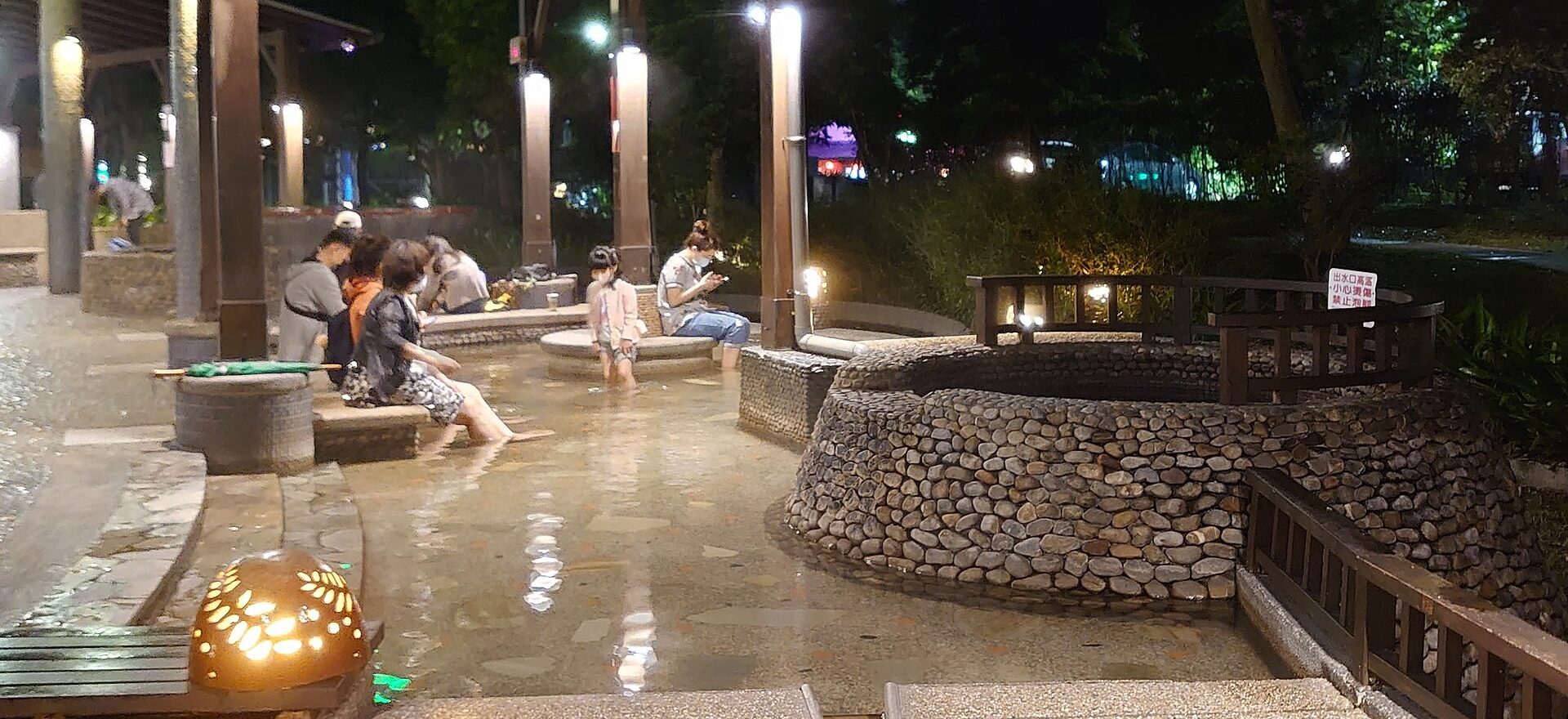 Visitors soaking their feet in the lit stone-lined foot baths of Jiaoxi Hot Spring Park at night