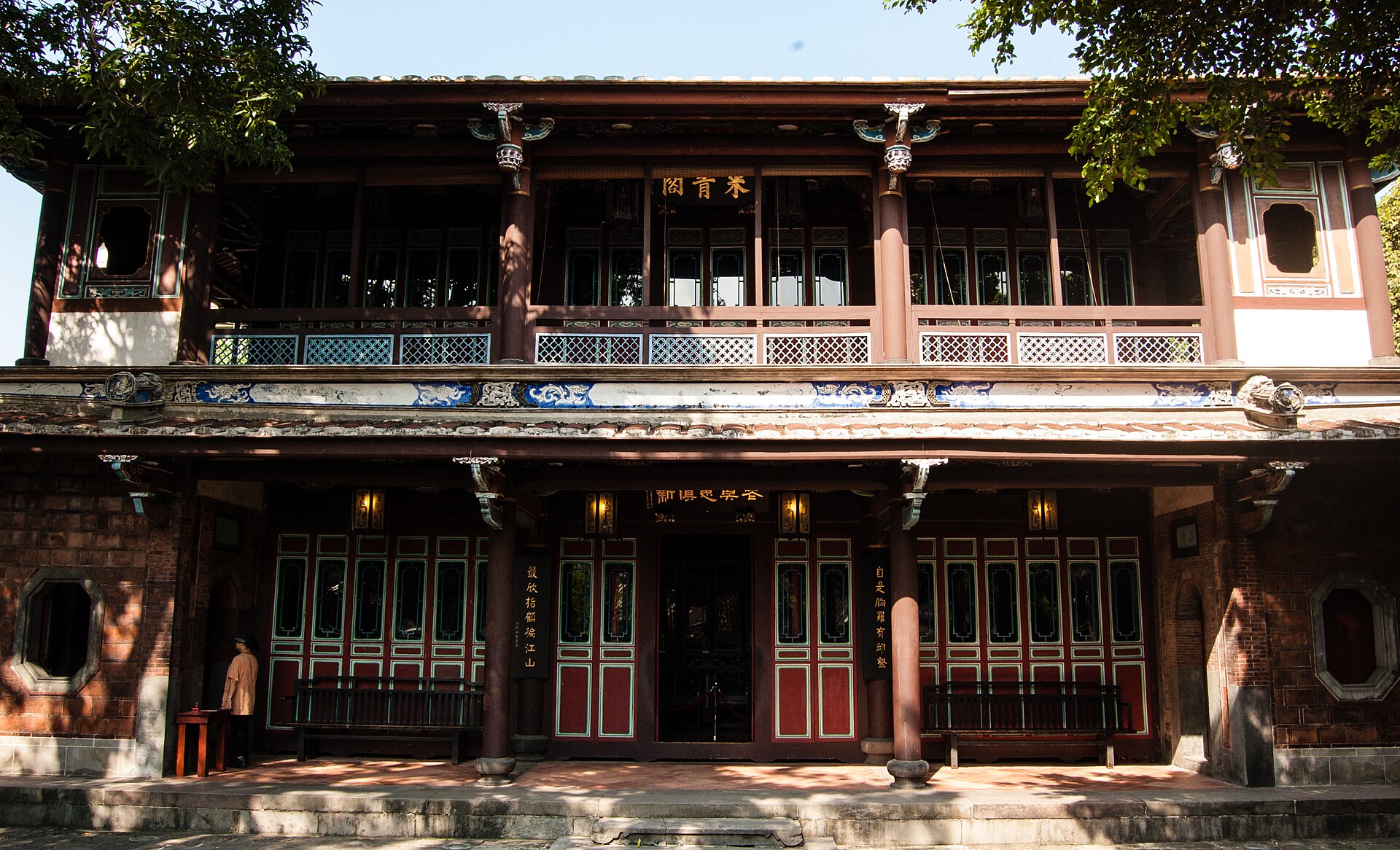 The two-storey Laiqing Pavilion in the Lin Family Garden, with carved balconies, lattice windows and a gold-lettered plaque, framed by trees