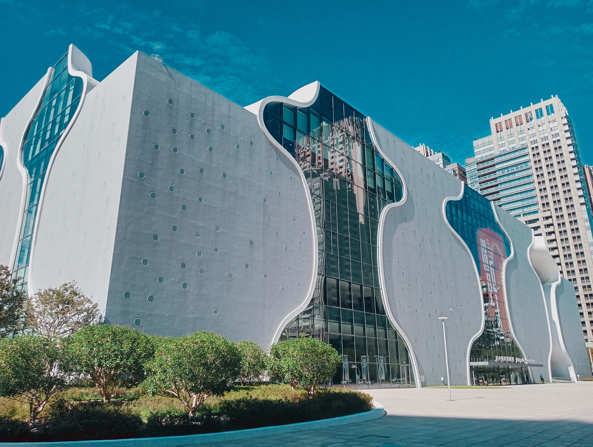 The curving concrete and glass facade of the National Taichung Theater against a blue sky