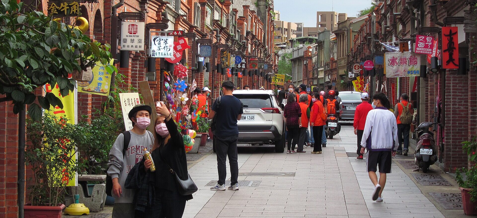 Visitors walking along Sanxia's Minquan Old Street between rows of restored red-brick shophouses with hanging shop signs