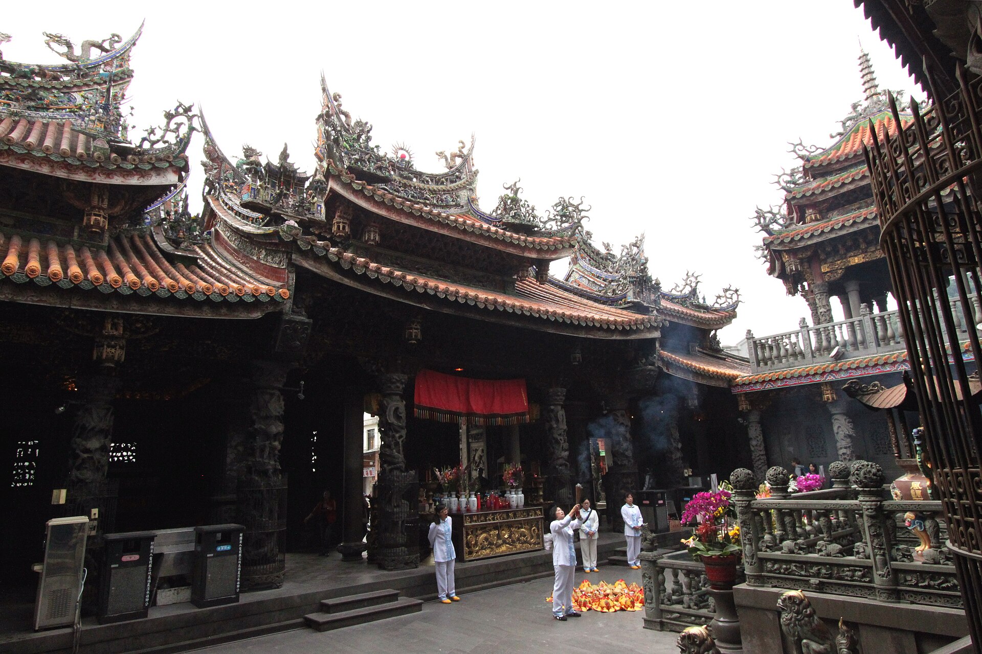 Worshippers in white holding incense in the courtyard of Sanxia's Zushi Temple, beneath layered roofs crowded with carved figures