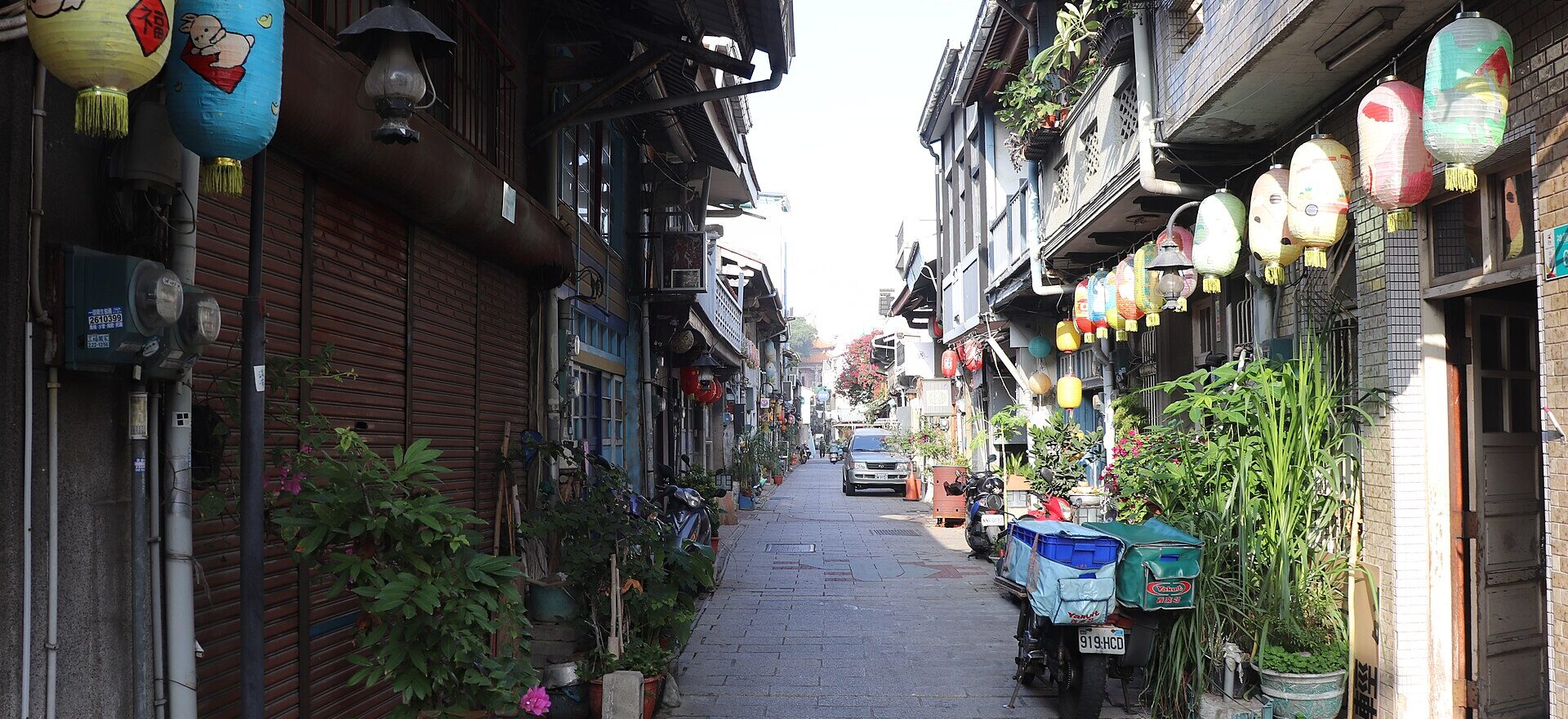 A narrow Tainan lane lined with restored shophouses, hanging paper lanterns and potted plants