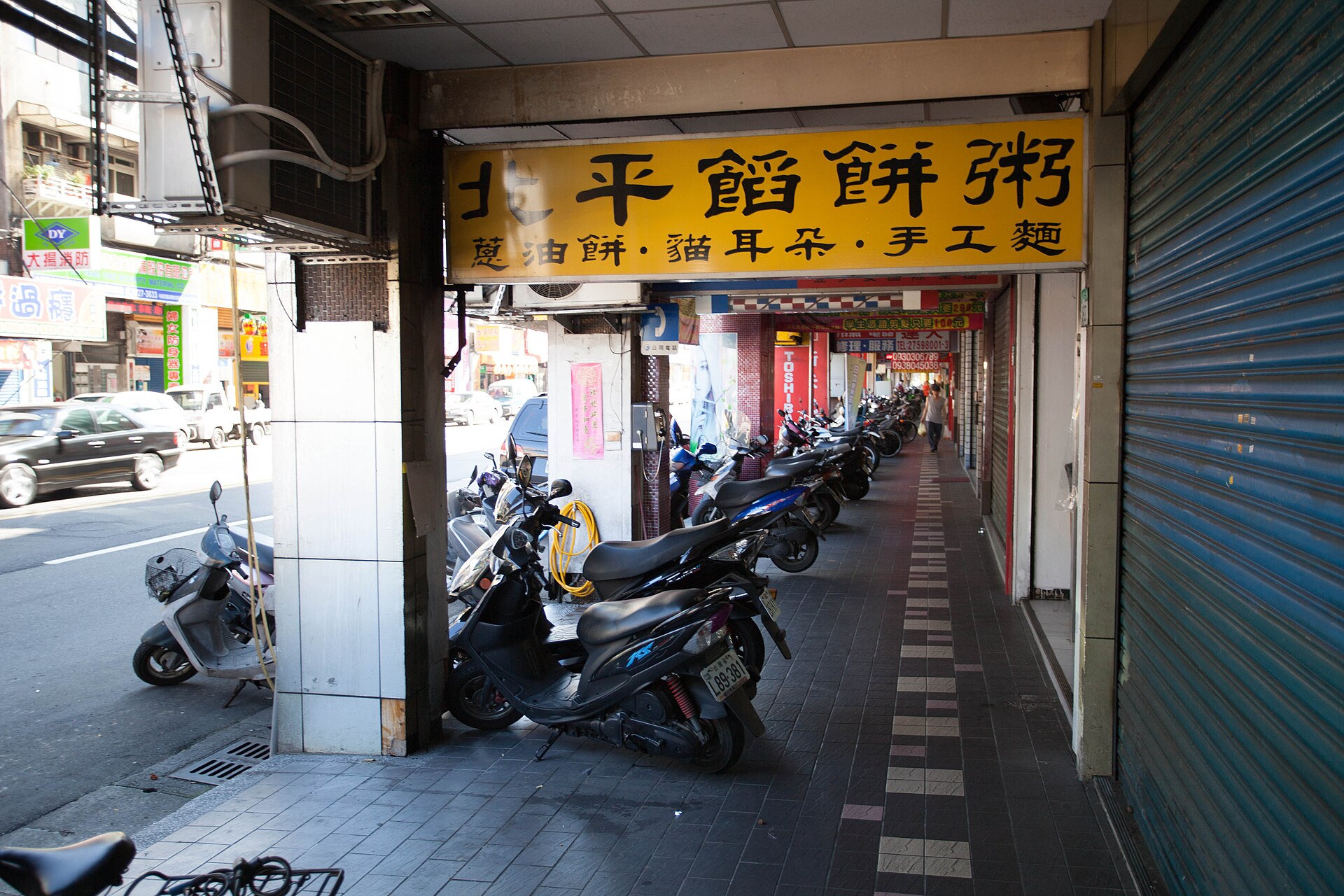 Scooters parked in a row along a covered arcade walkway in Taipei, narrowing the passable width
