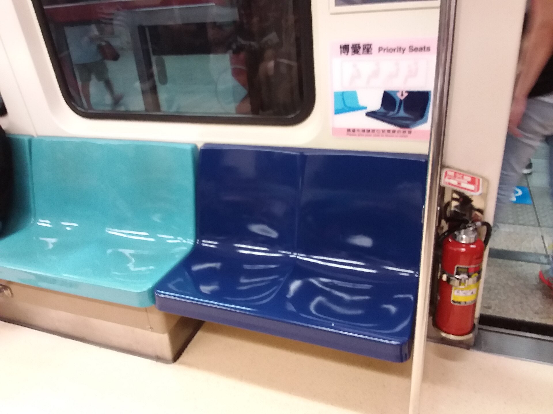 Dark blue priority seats next to ordinary teal seats in a Taipei Metro carriage, with a bilingual priority seat sign above