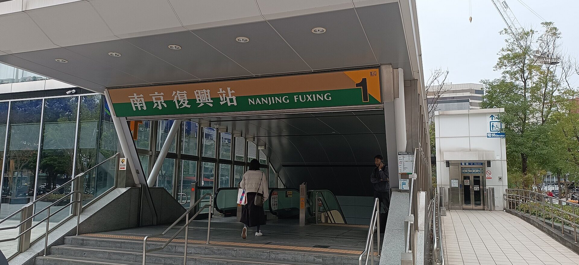 Street-level accessible lift beside the stepped Exit 1 entrance at Nanjing Fuxing MRT station