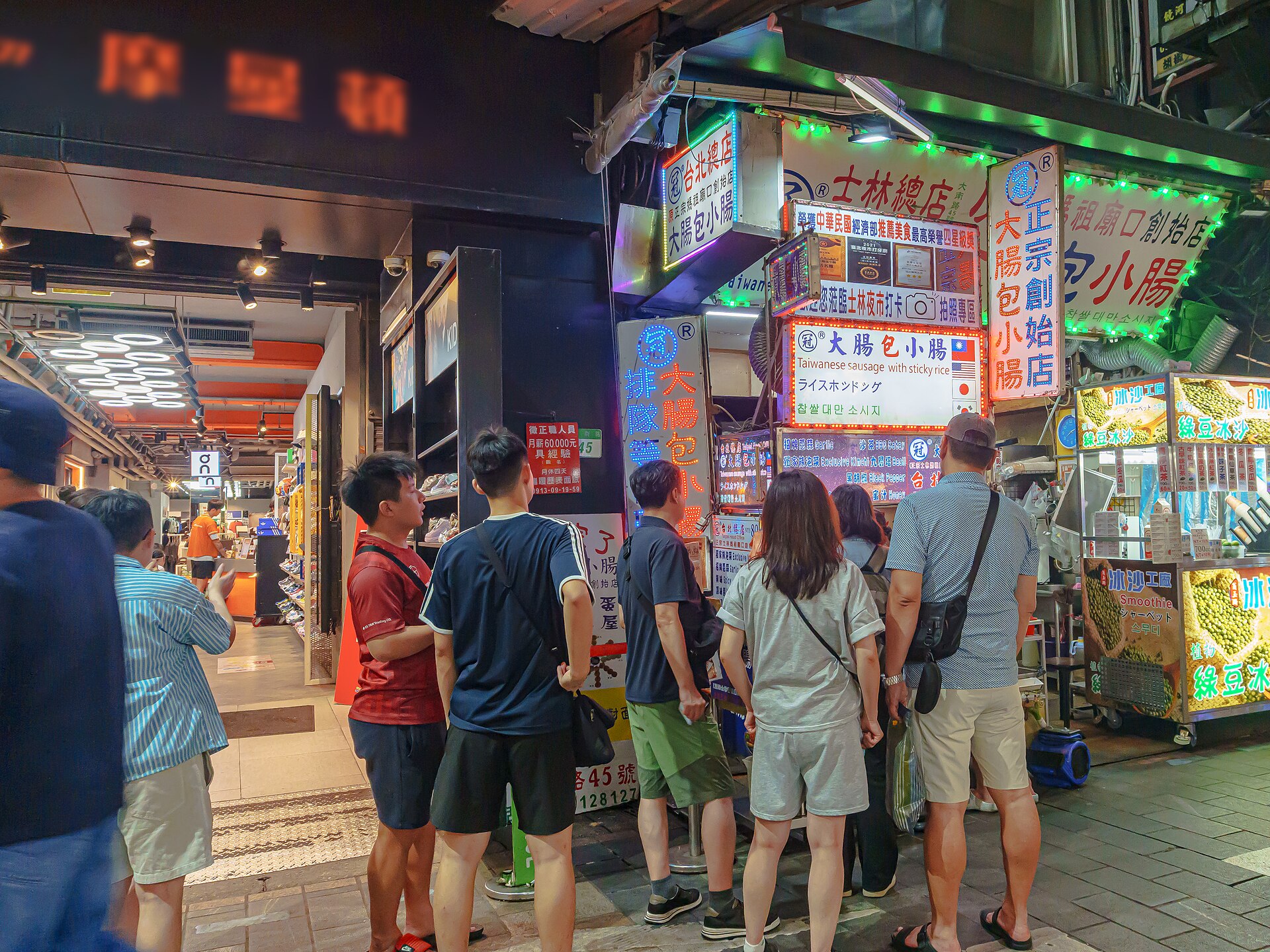 Customers queuing at a night market food stall in Taipei with a handwritten price board