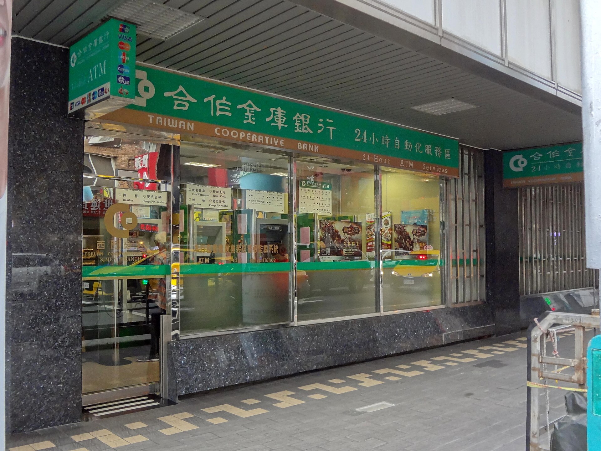A 24-hour bank ATM lobby in Taiwan with international card network logos on the sign
