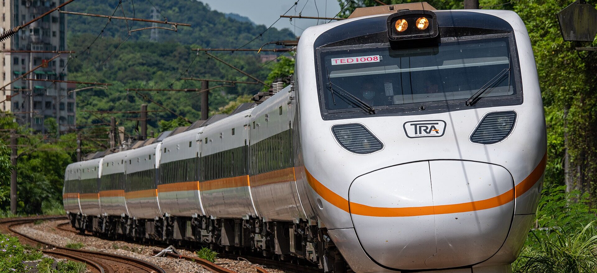 A white Taroko Express tilting train with an orange stripe rounding a curve between green hills