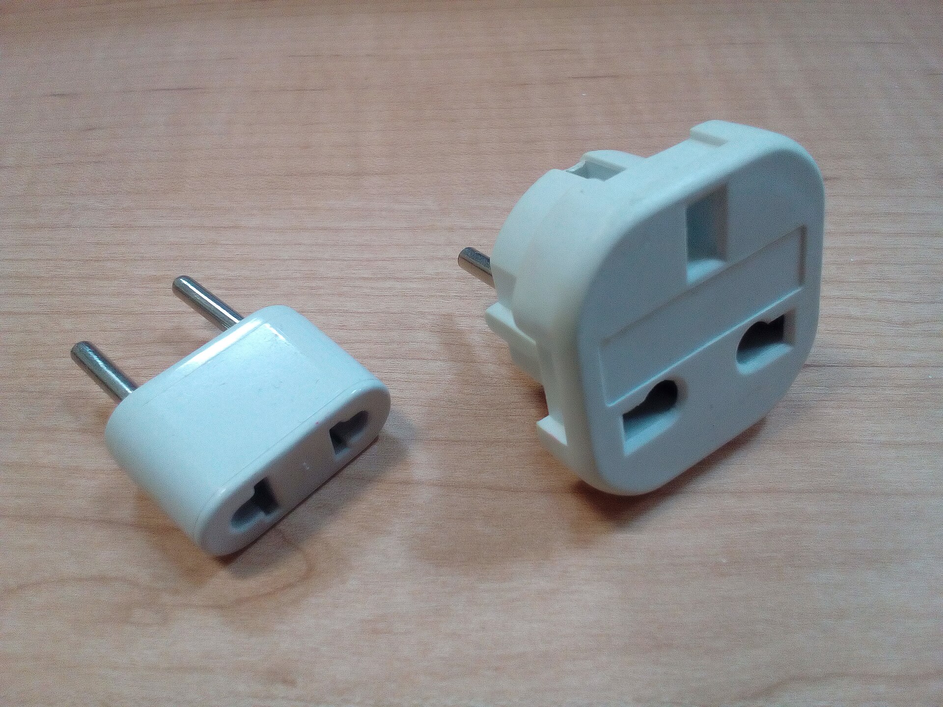 Two white travel plug adapters on a wooden table