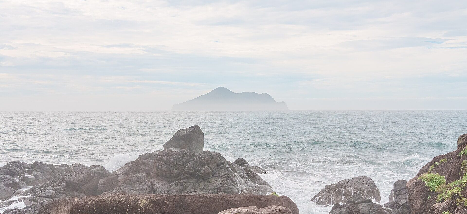 Turtle Island rising from a hazy sea beyond dark wave-washed rocks on the Toucheng shore