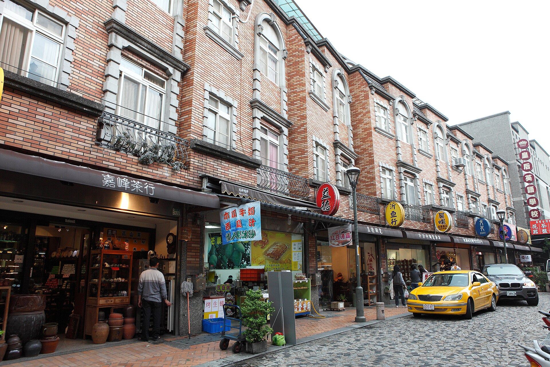 Brick shop buildings with arched windows lining a cobbled street in Yingge, with a tea shop and pottery on display