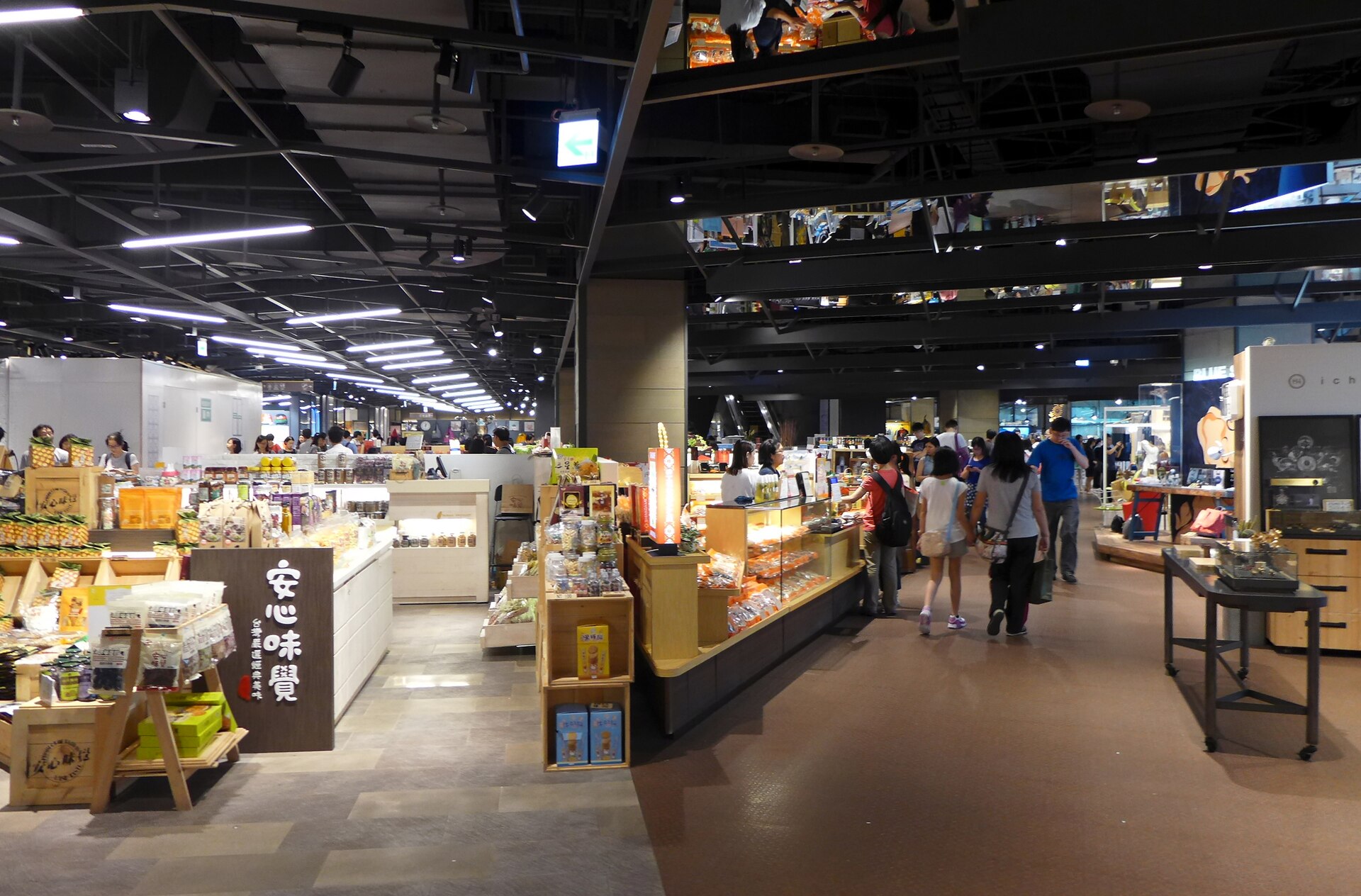 Busy aisle inside Eslite Spectrum Songyan in Taipei, with shoppers passing wooden counters of packaged snacks and gifts under a dark ceiling.
