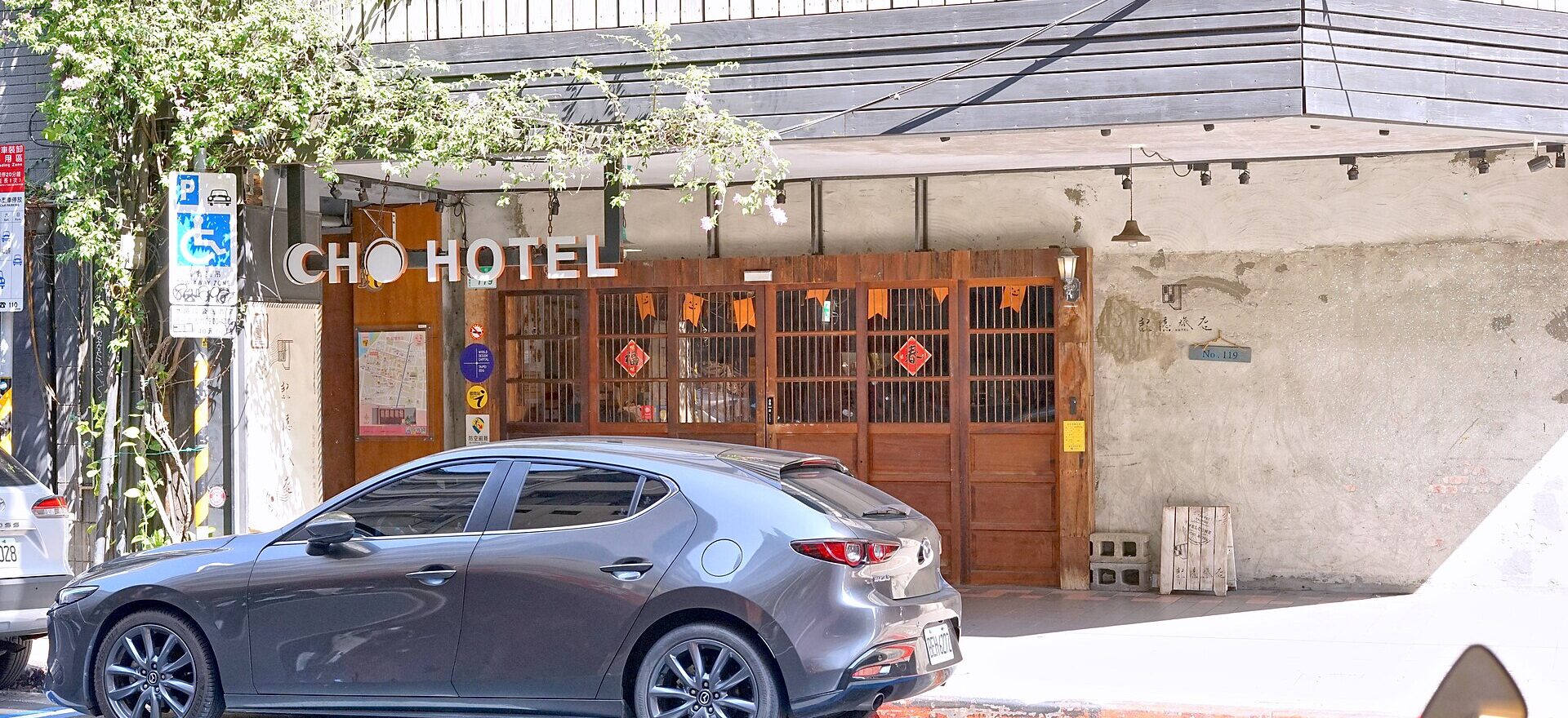 Cho Hotel in Taipei has wooden entrance doors, hanging greenery and large white lettering above a car parked outside.