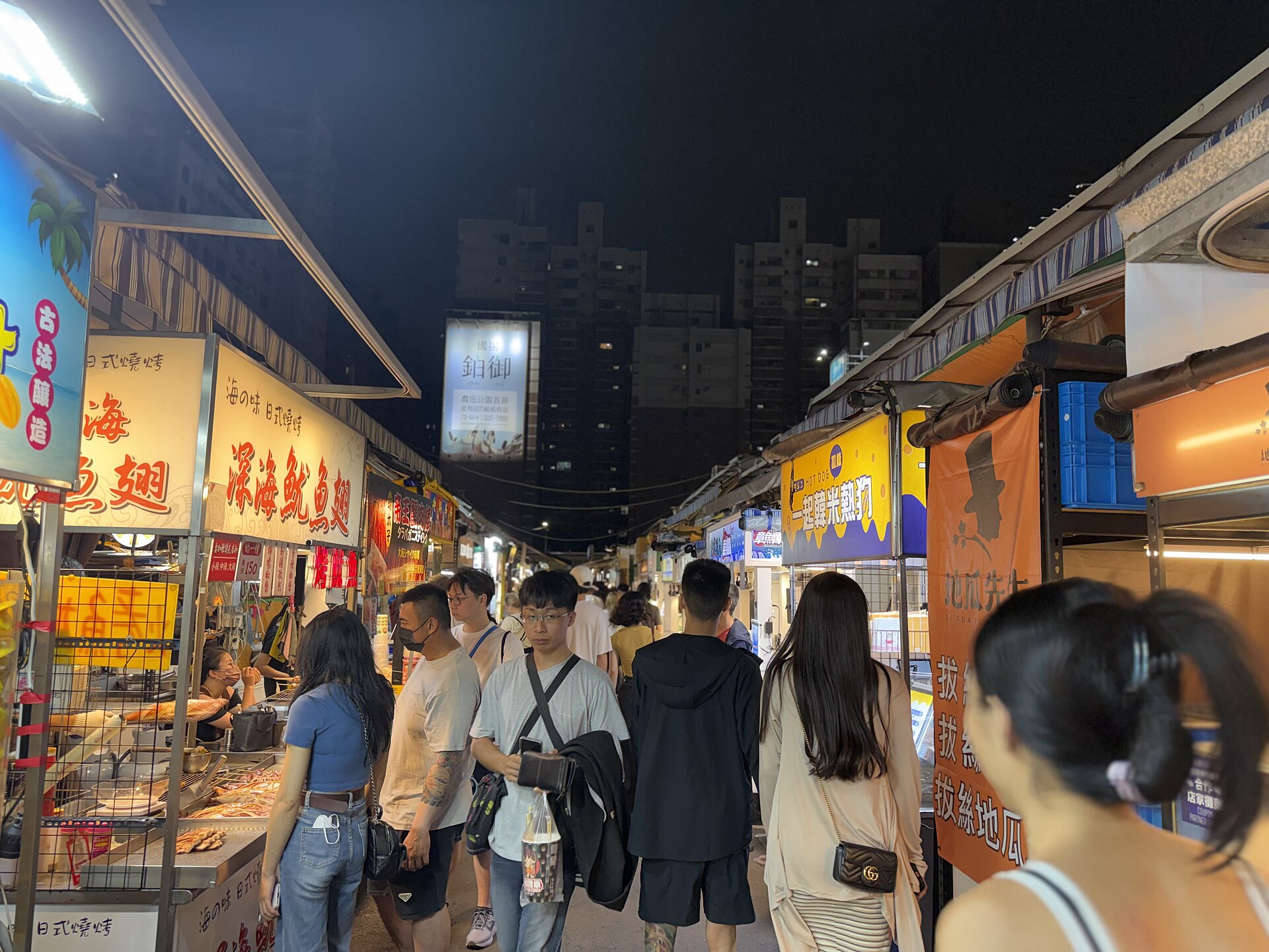 Crowds fill a narrow aisle between brightly lit food stalls at Ruifeng Night Market in Kaohsiung after dark.