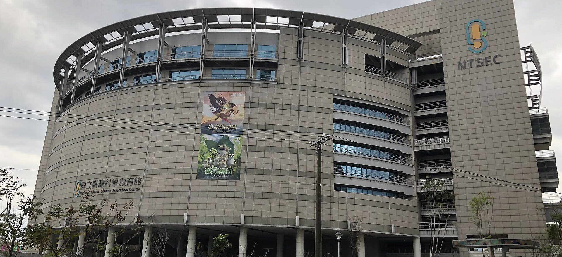 The curved National Taiwan Science Education Center building stands beside a Taipei street under an overcast sky.