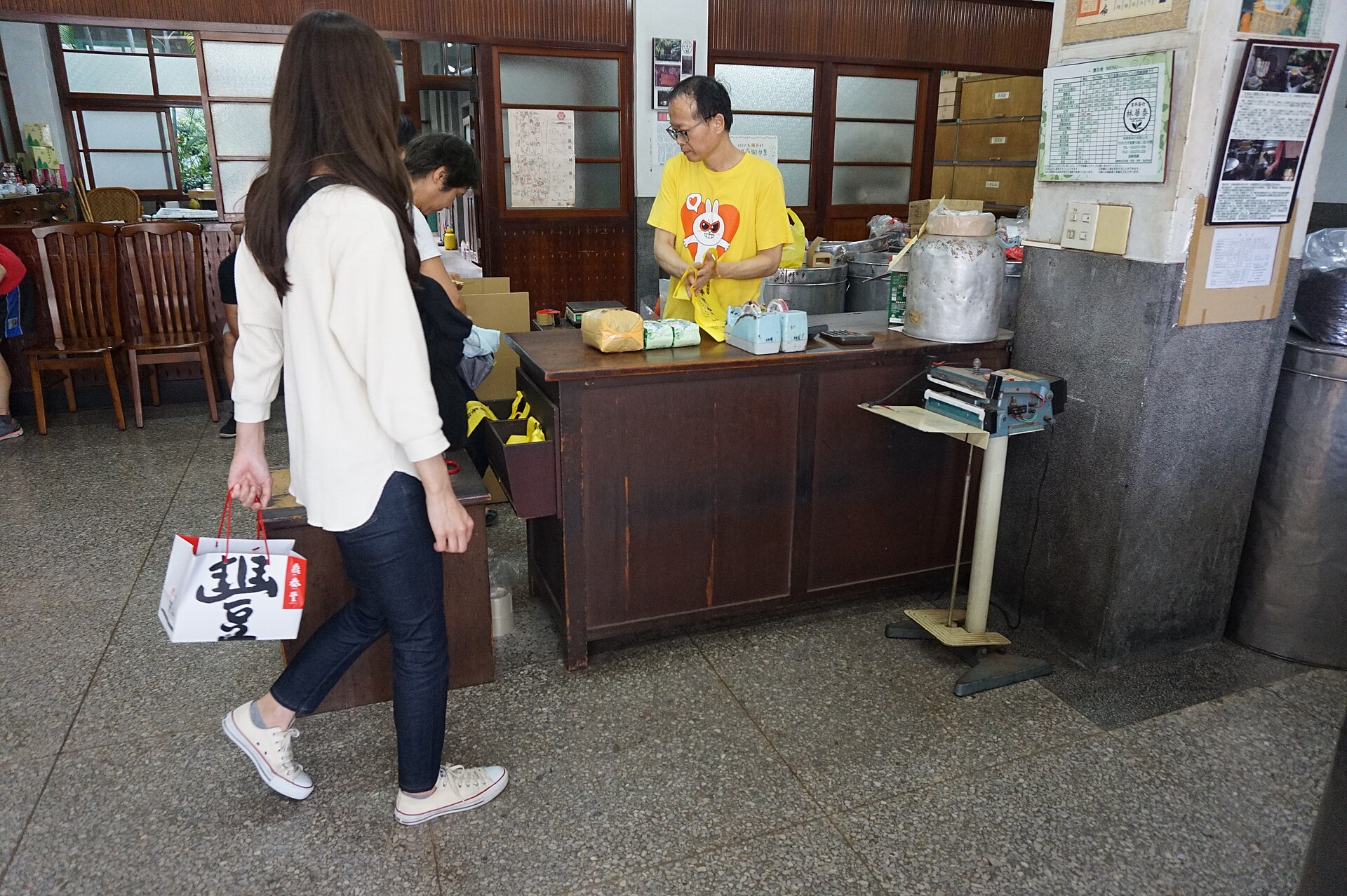 Customers approach a wooden counter with tea packages and metal tins at Lin Hua Tai Tea Shop in Taipei.