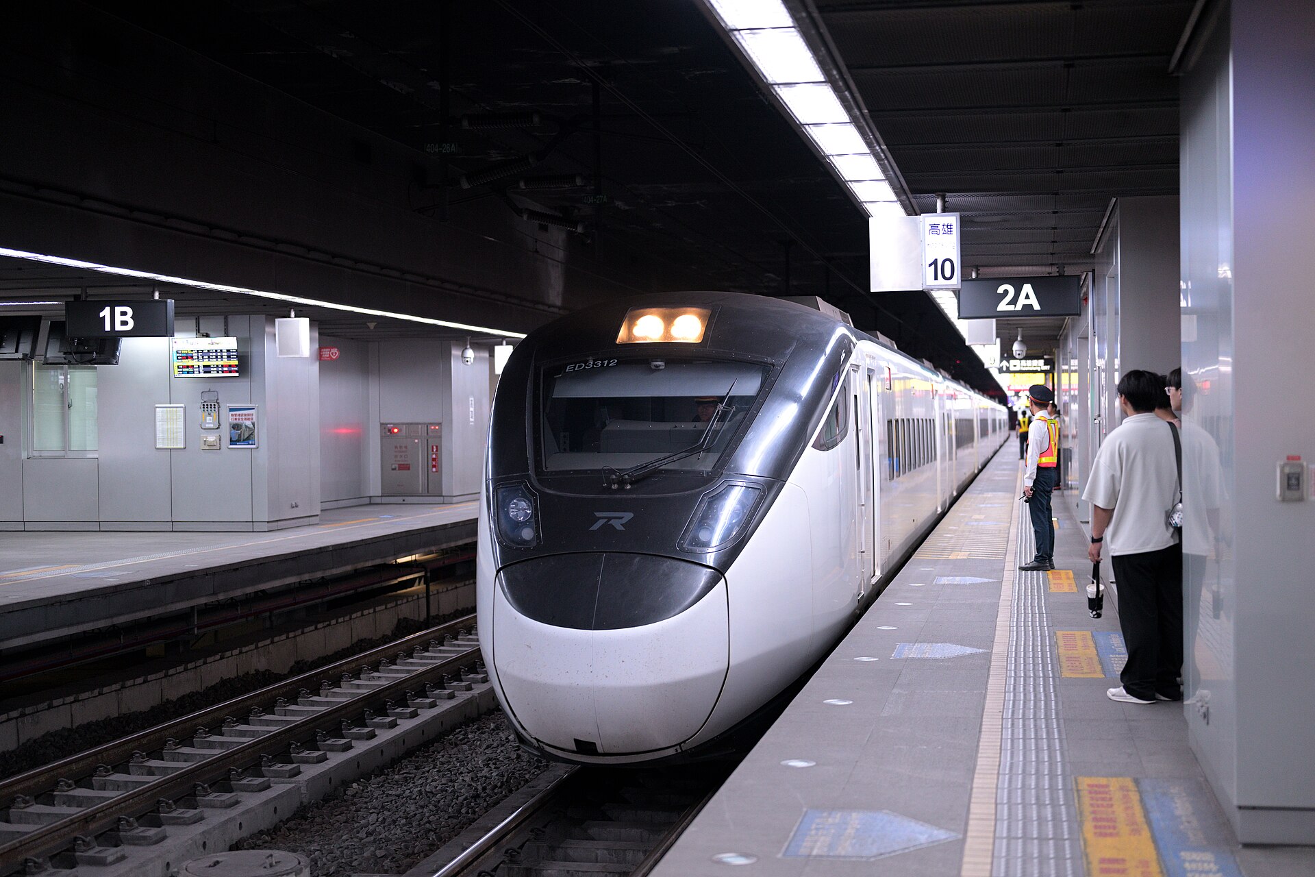 An EMU3000 express train approaches the underground platform at Kaohsiung station, with adults waiting behind the platform edge.