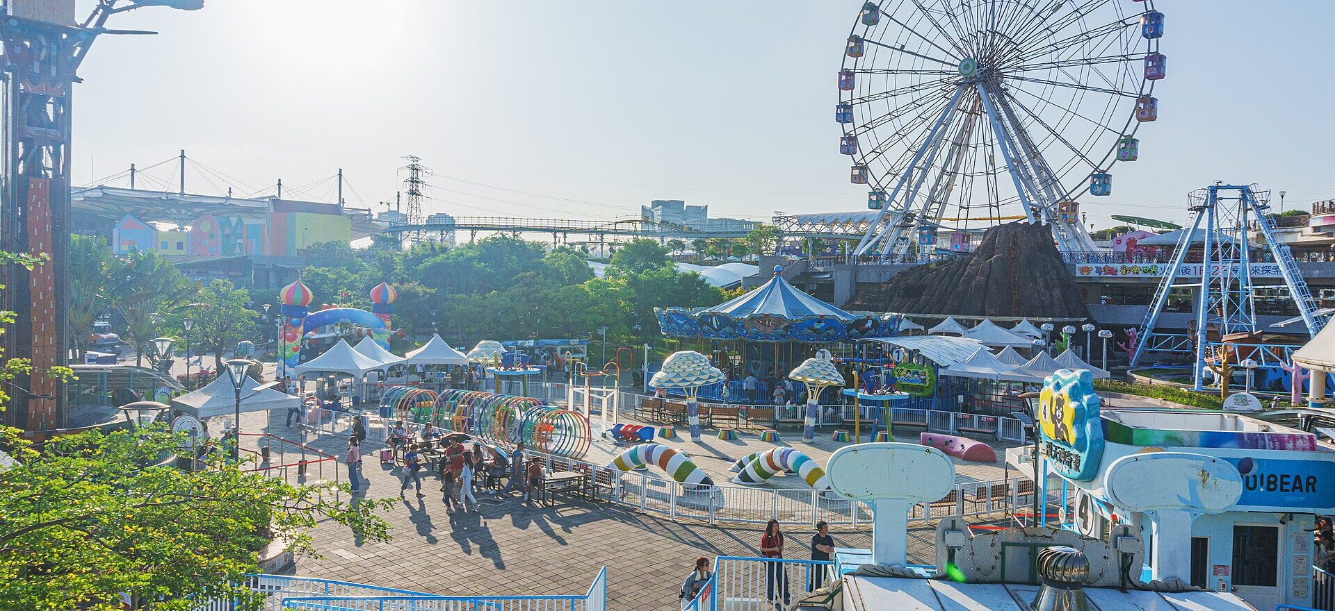 The Ferris wheel rises over colorful rides and visitors at Taipei Children's Amusement Park in afternoon sunshine.