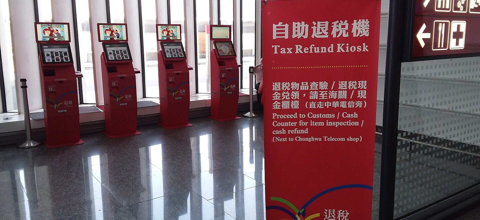 Four red tax refund kiosks stand beside a bilingual instruction banner inside Taoyuan Airport Terminal 1.