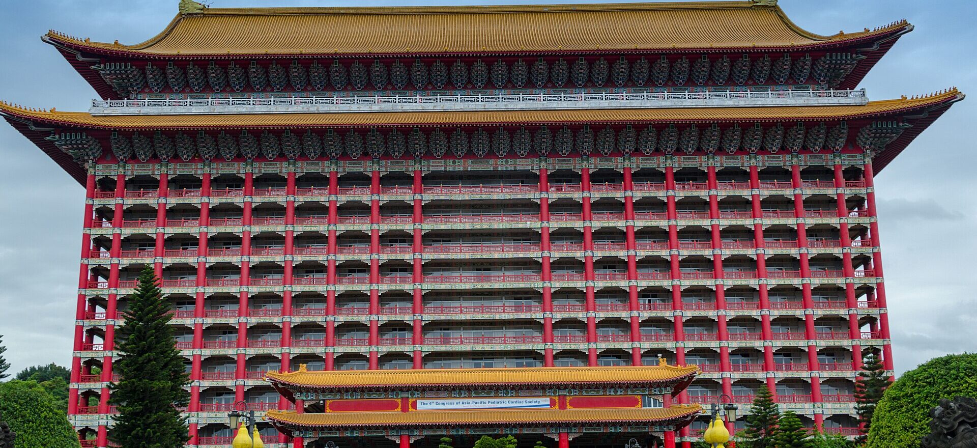 The Grand Hotel in Taipei rises above its entrance gardens, with red columns, gold roofs and visitors on the steps.