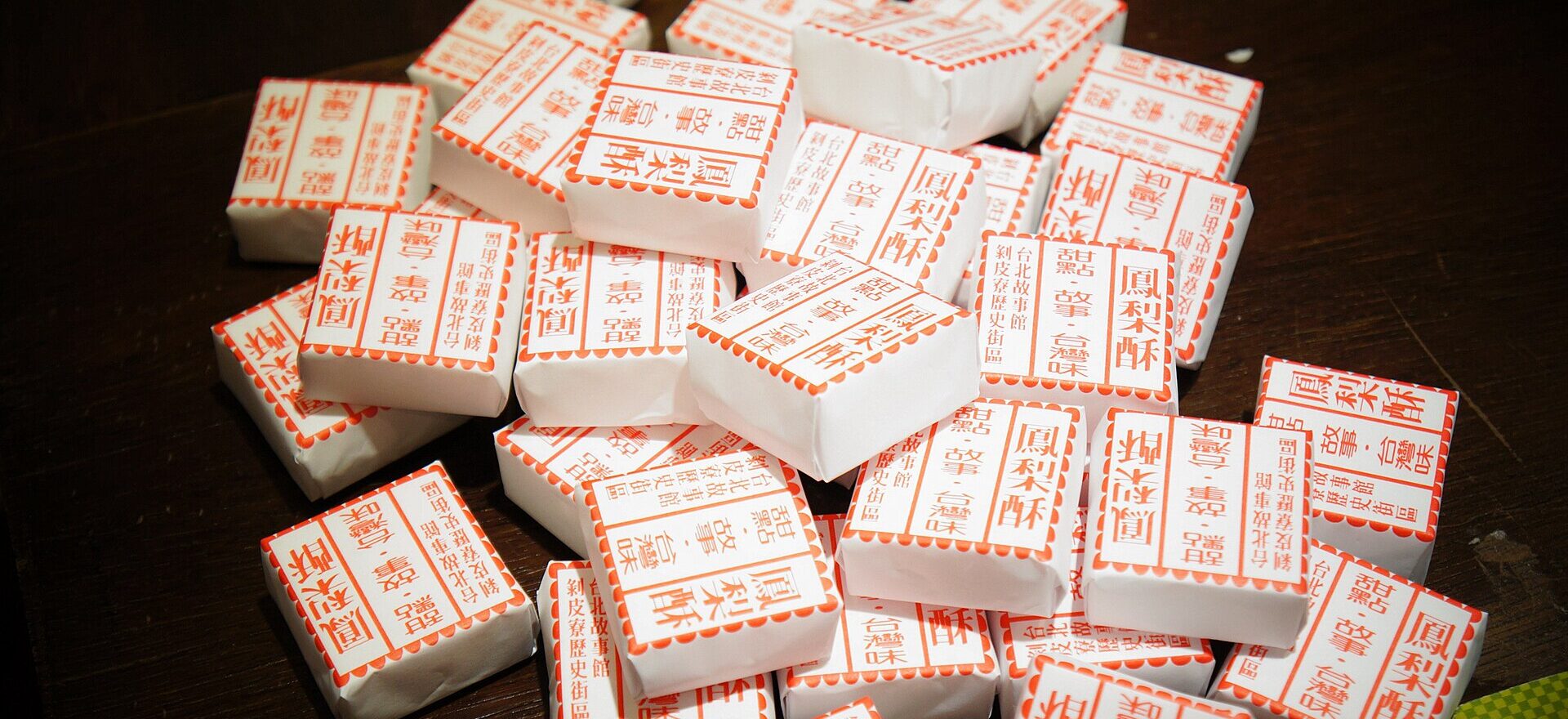 Individually wrapped pineapple cakes with red Chinese lettering are piled on a dark table at Taipei Story House.