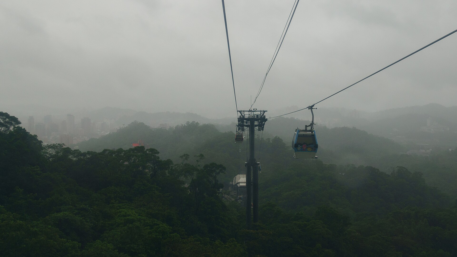 Maokong Gondola cabins cross wooded hills above Taipei, with cable towers and distant buildings softened by mist.