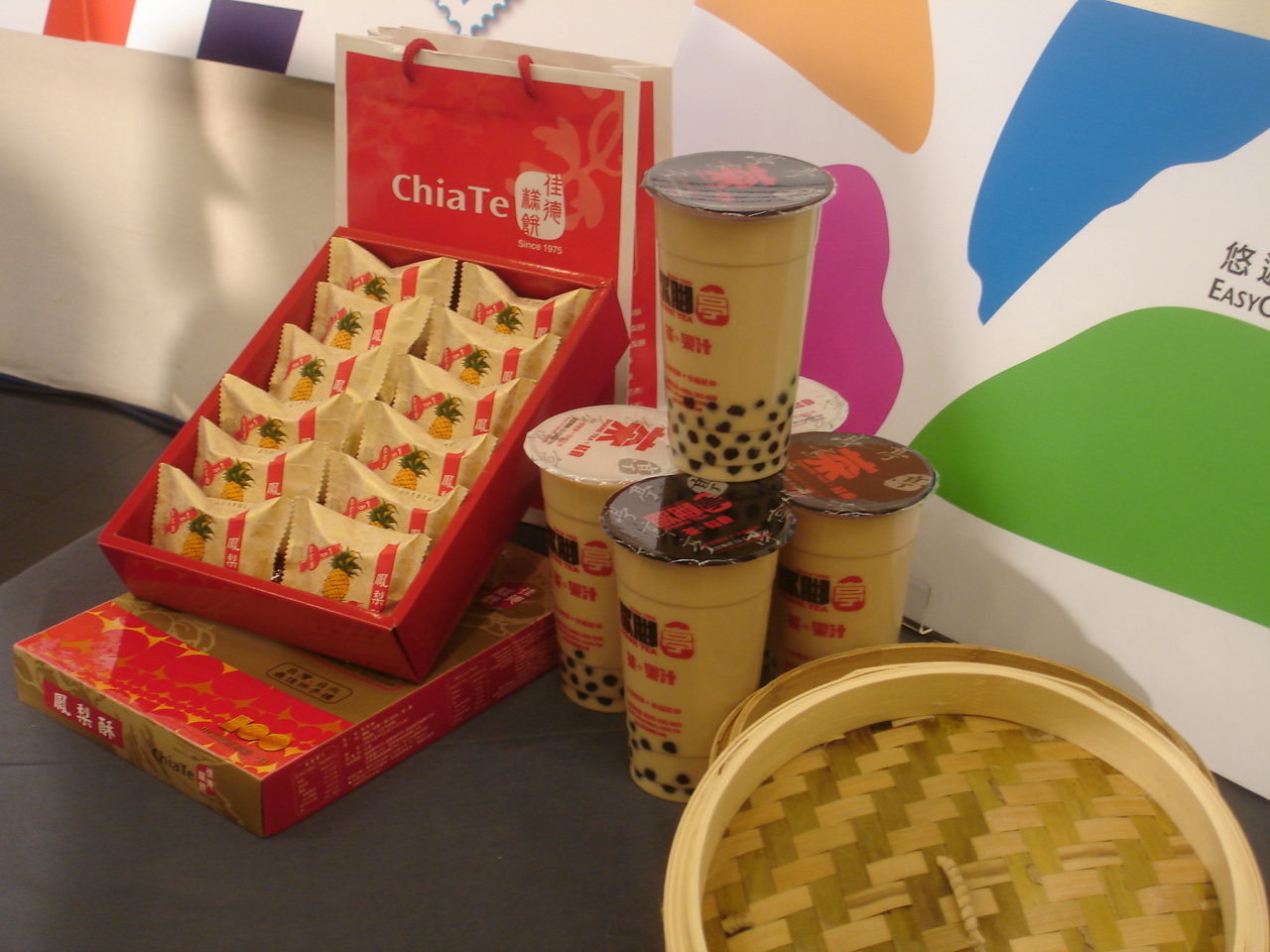 An open Chia Te pineapple cake gift box and matching bag stand beside bubble milk tea in a Taipei display.