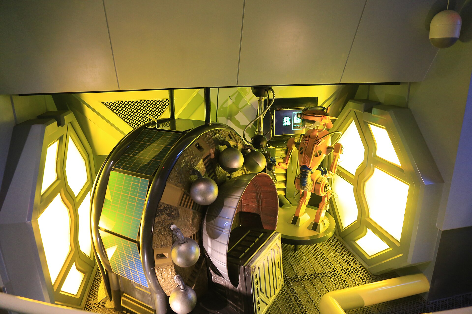 An orange robot figure stands beside a large mechanical wheel in a yellow-lit National Taiwan Science Education Center display in Taipei.