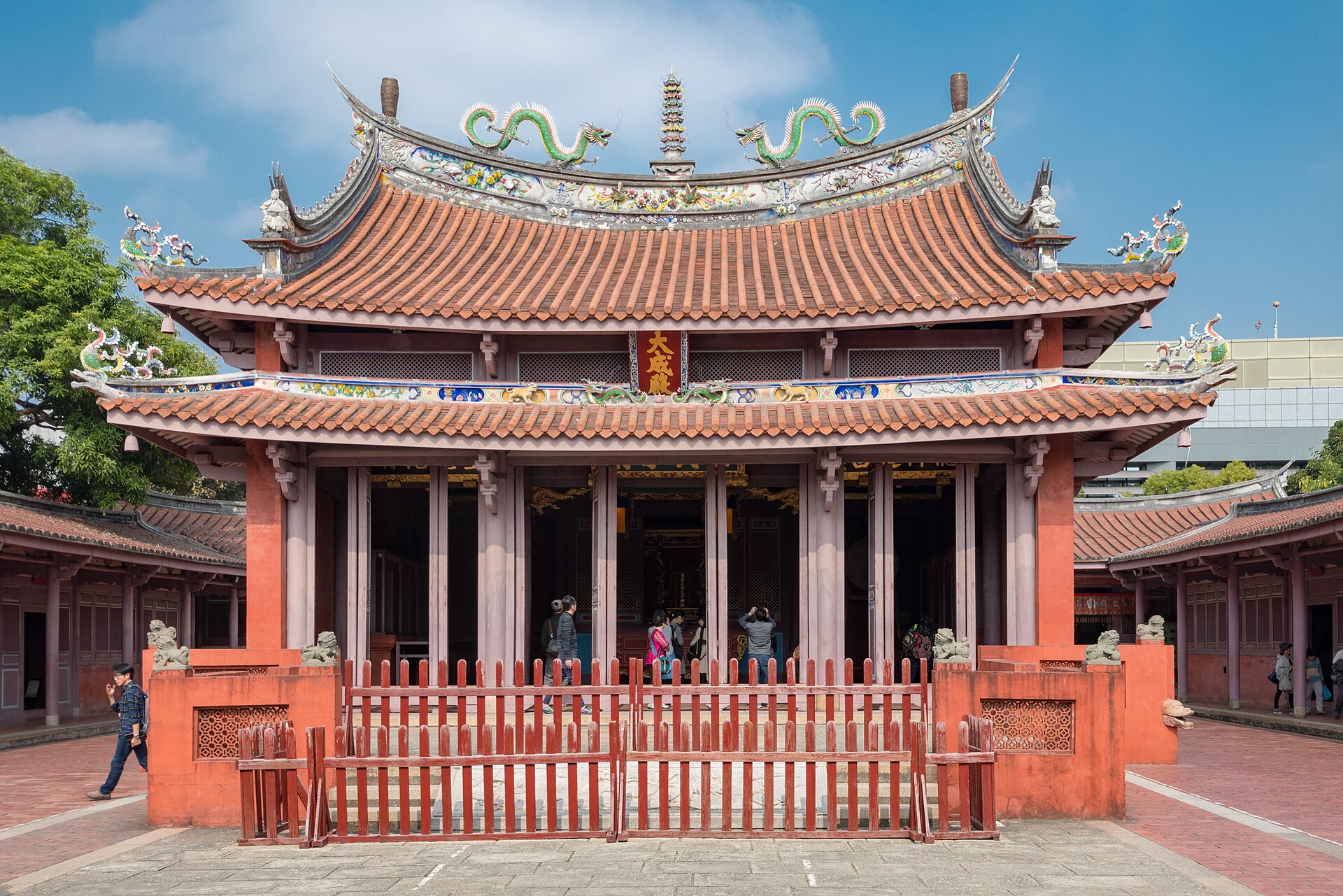 Paired green dragons crown the tiled roof of Tainan Confucius Temple above visitors and a red courtyard fence.