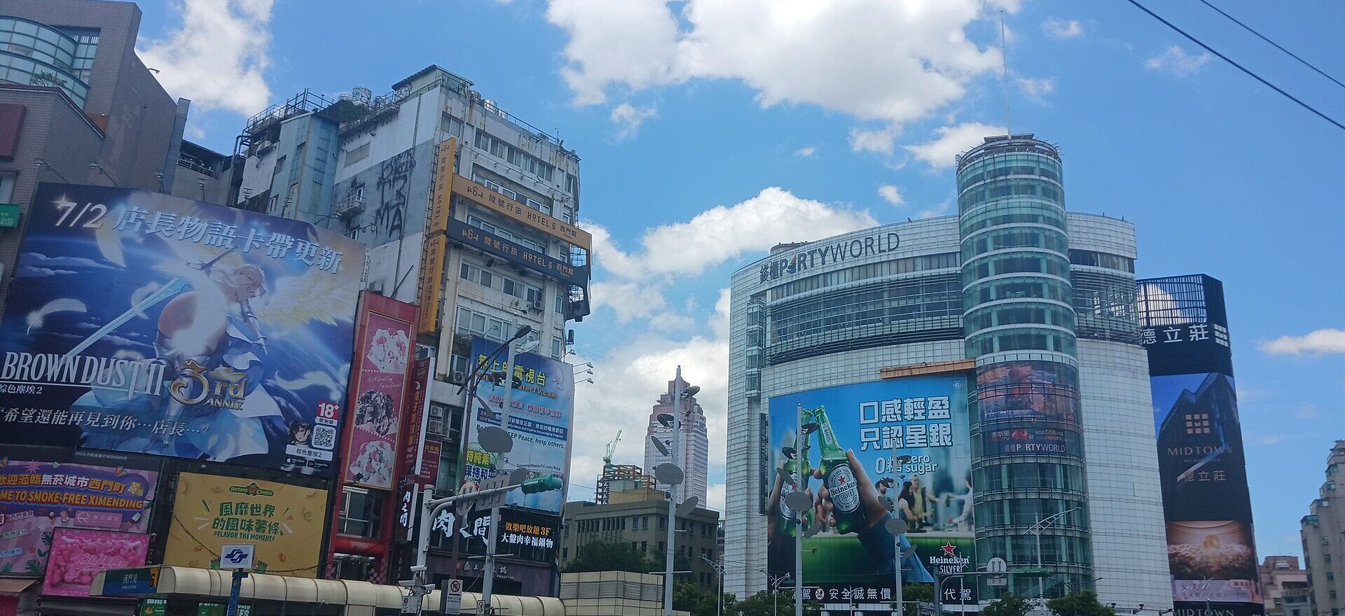 Partyworld karaoke building beside a busy Taipei intersection, with a cylindrical glass tower and large advertising panels.