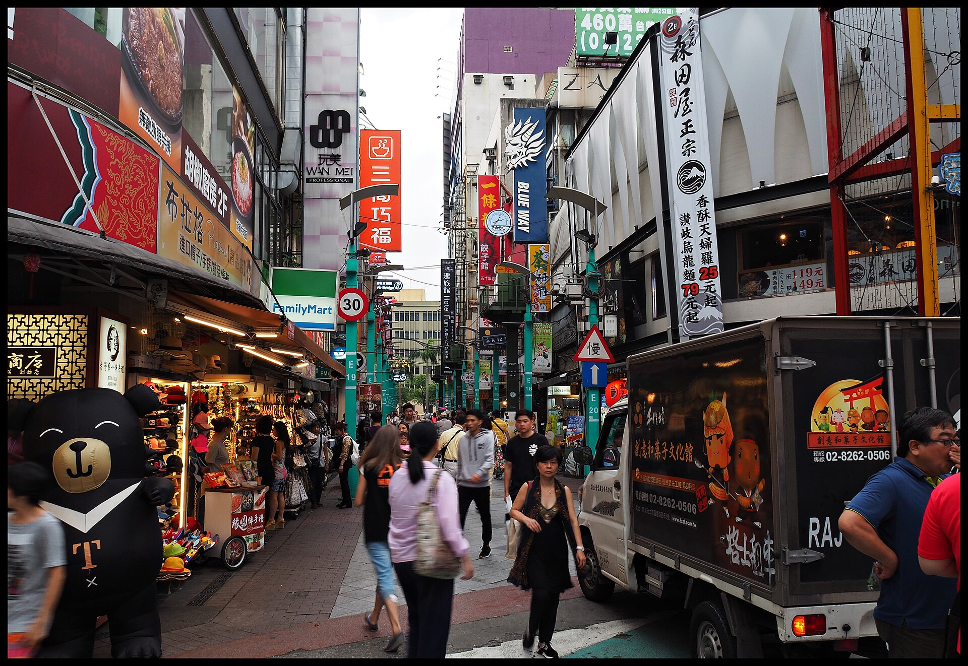 Pedestrians pass closely packed shops and vertical signs along a narrow shopping lane in Taipei's Ximending district.