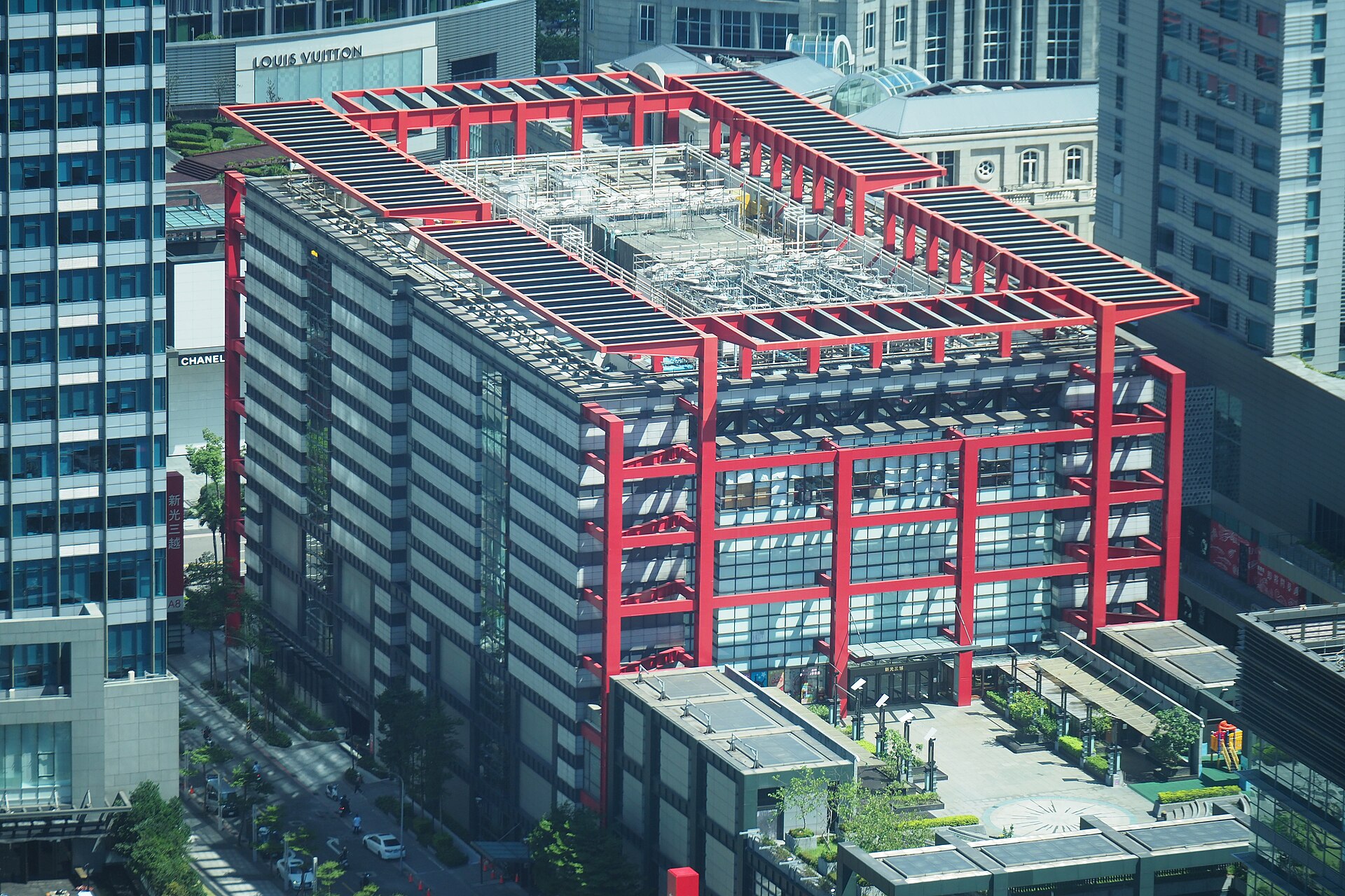 Shin Kong Mitsukoshi Xinyi Place A8 in Taipei has a red structural frame surrounded by tall buildings and elevated walkways.