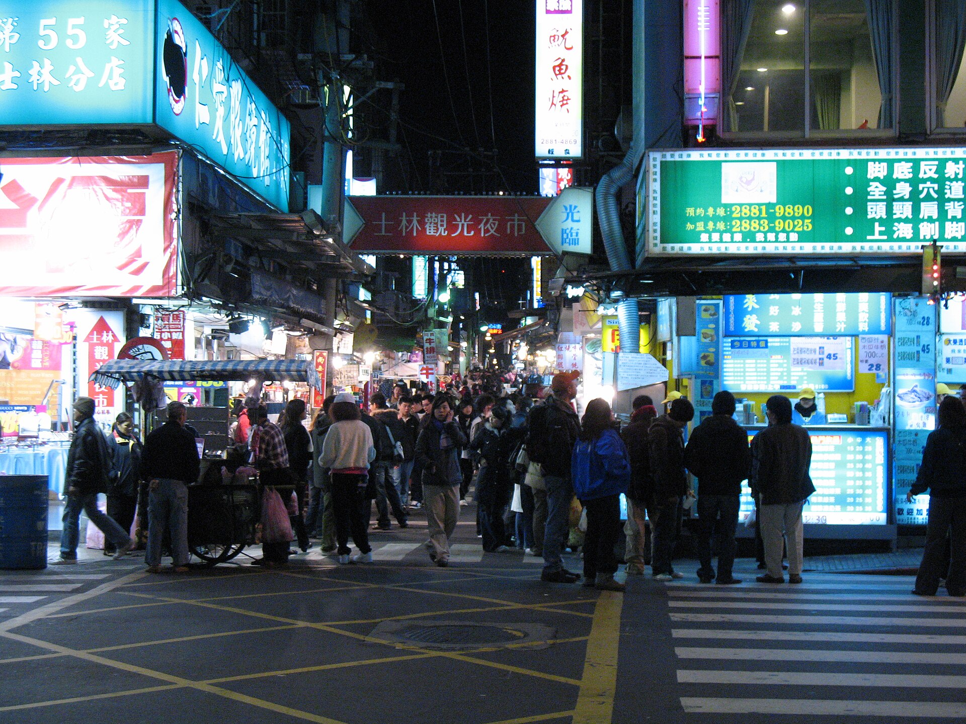 Shoppers crowd the brightly lit entrance to a Shilin Night Market lane in Taipei beneath an overhead market sign.