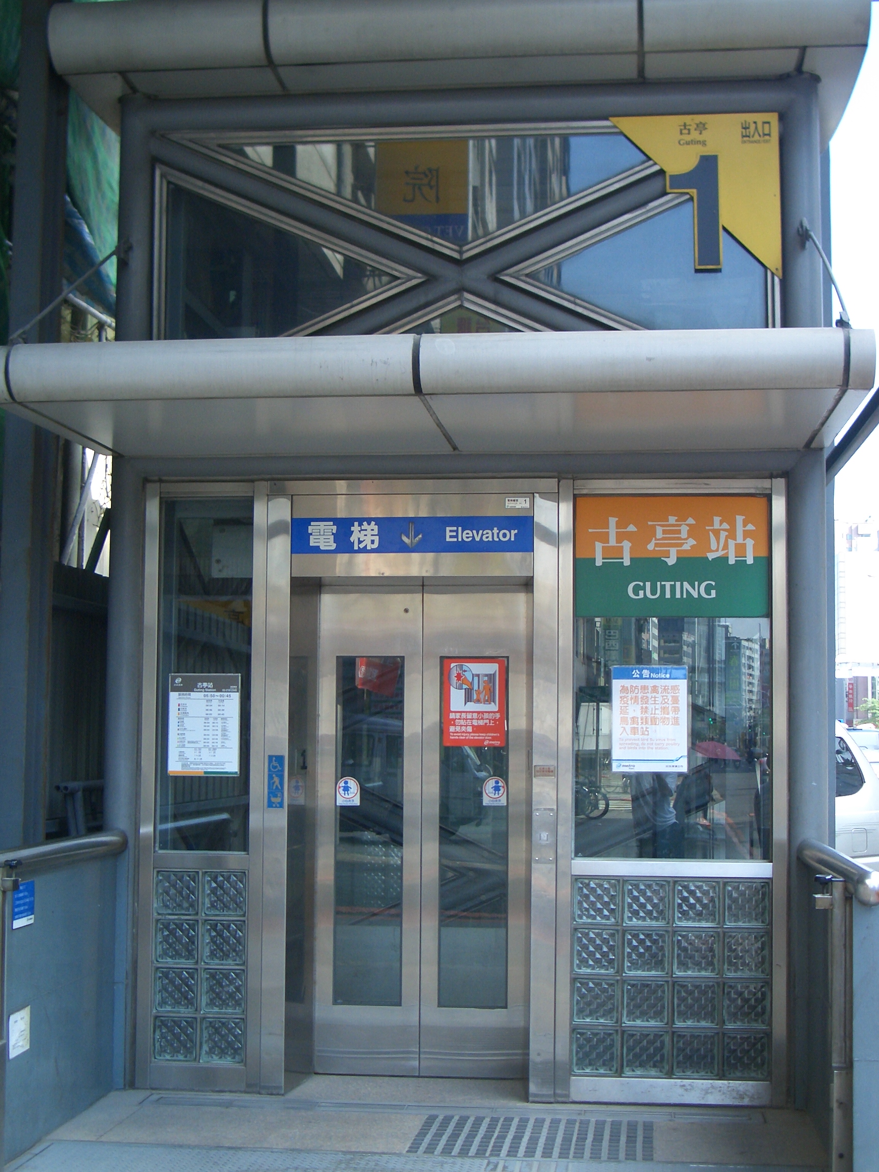 Street-level elevator at Taipei MRT Guting station Exit 1, with glass walls and tactile paving outside.