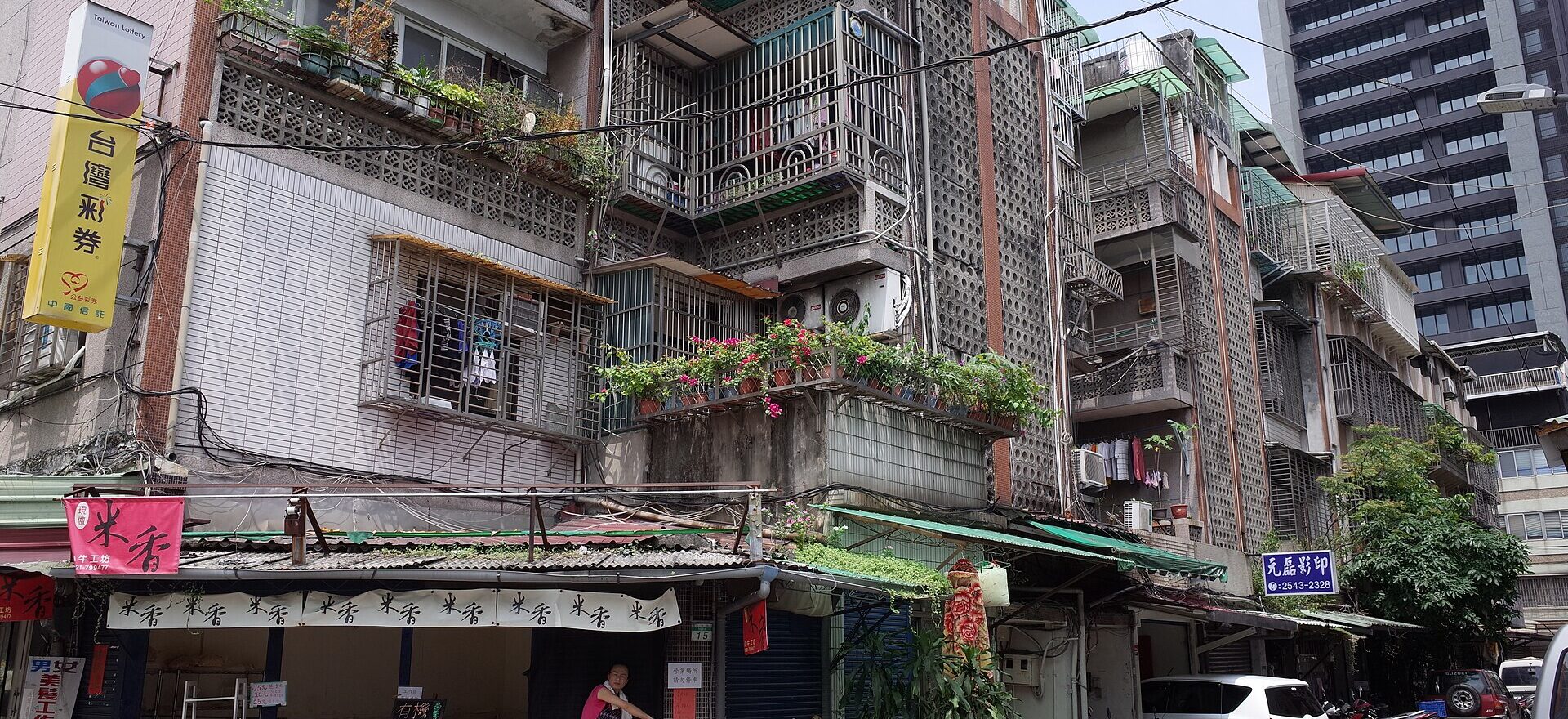 Taipei apartment buildings have tiled walls, enclosed balconies and air conditioners above small street shops and parked scooters.