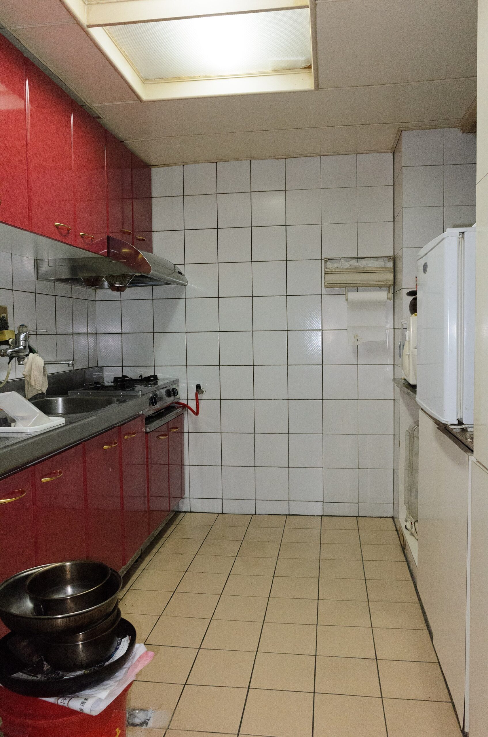 A Taipei apartment kitchen has red cabinets, white tiled walls, a stainless steel sink and a gas hob.