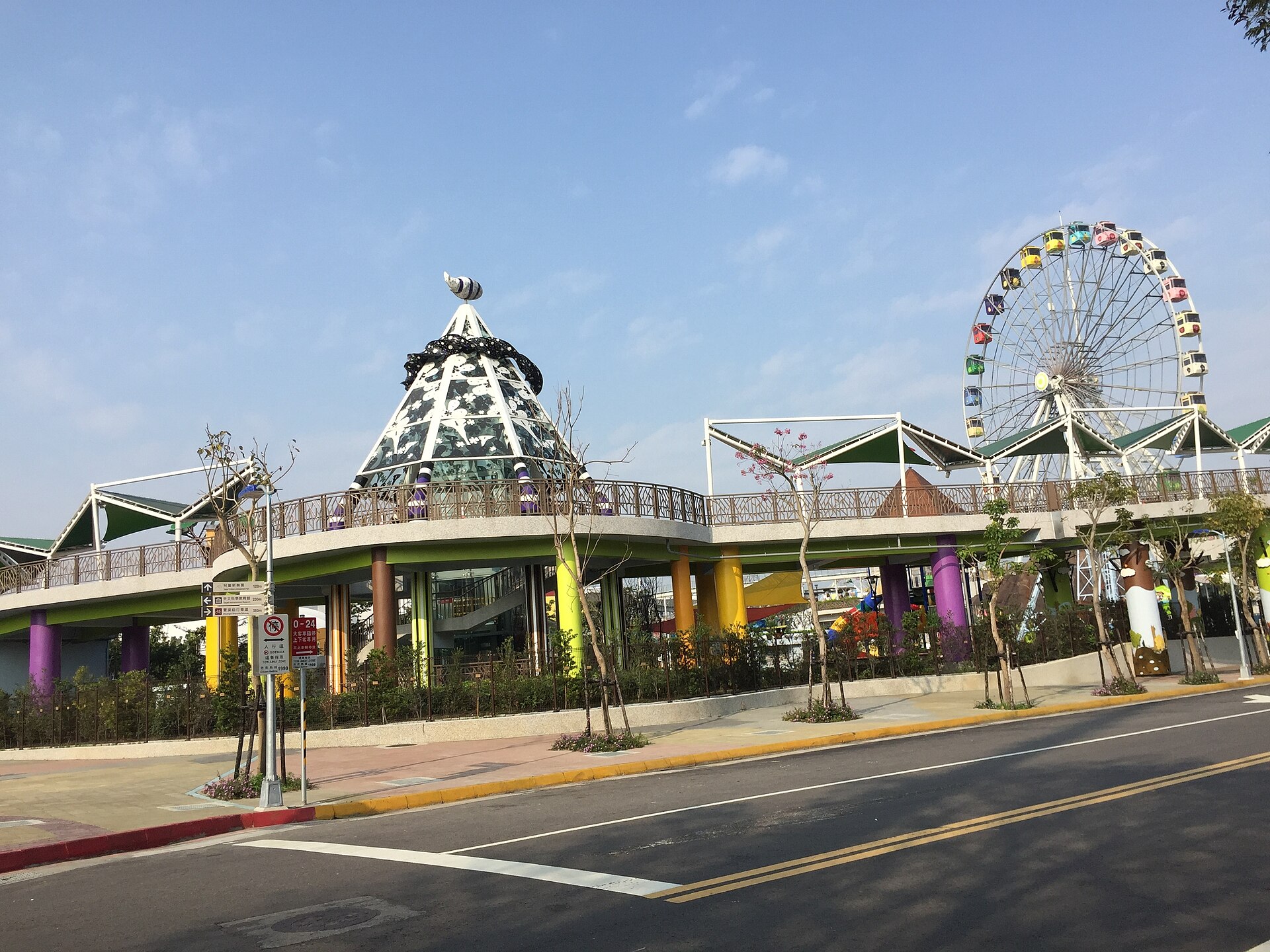 Taipei Children's Amusement Park's Ferris wheel stands behind a raised walkway with colorful columns beside the street.