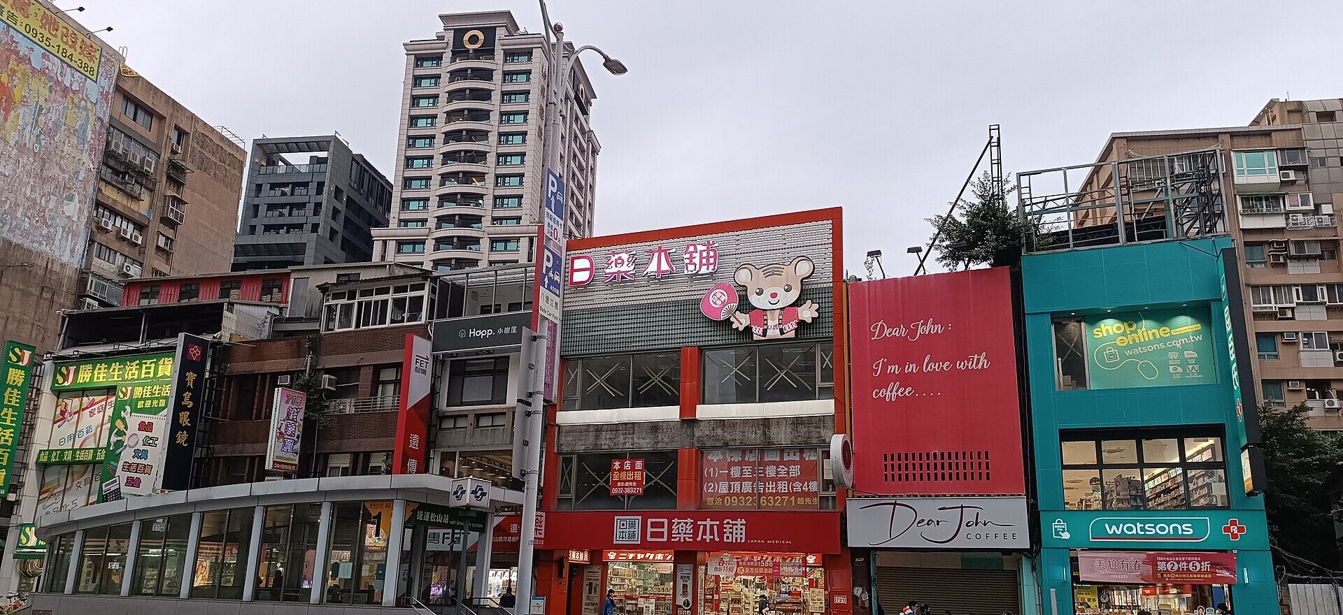 A turquoise Watsons drugstore stands beside neighboring shops on Taipei's Bade Road, with pedestrians outside the brightly lit entrance.