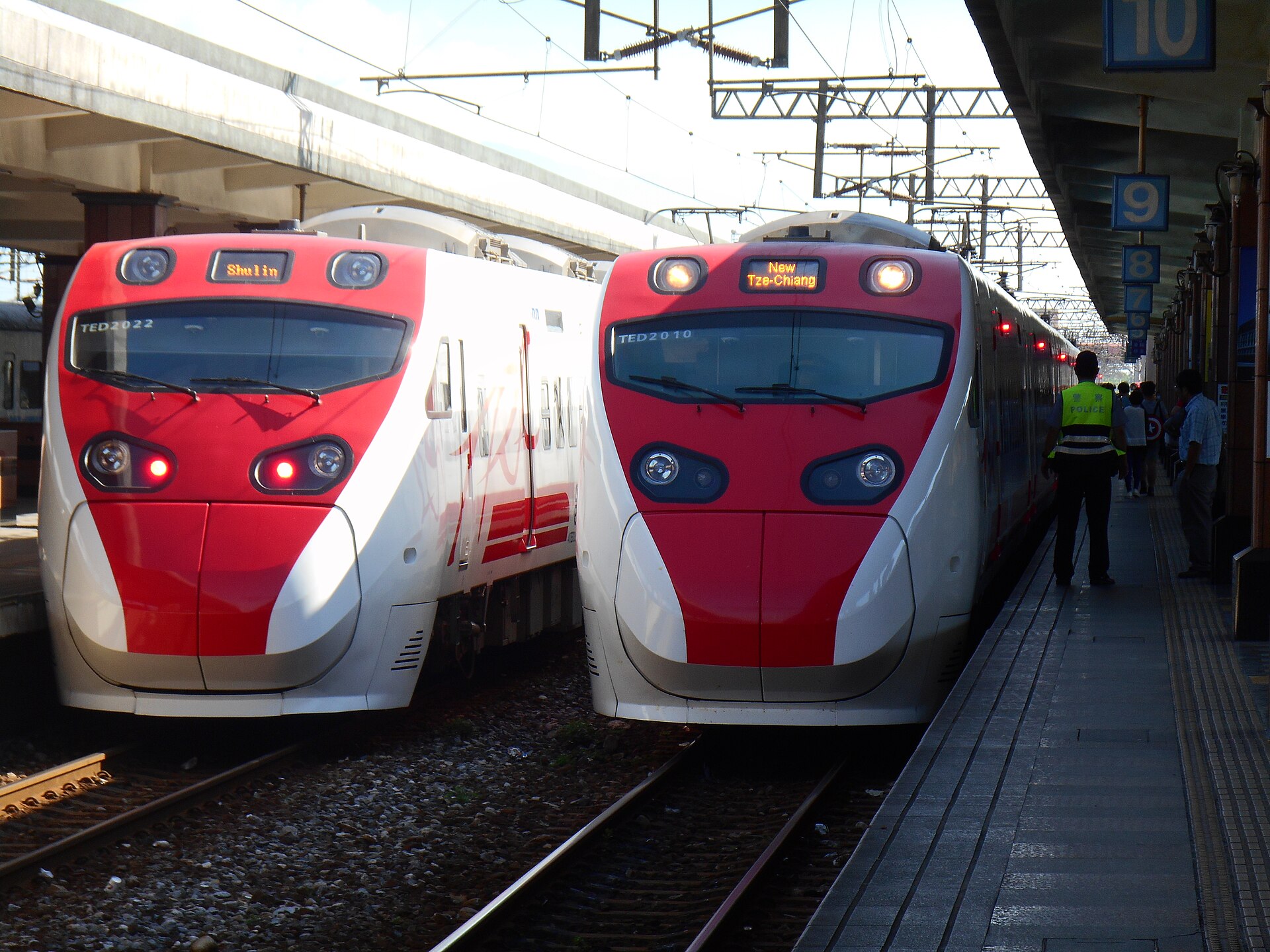 Two red and white Puyuma express trains stand side by side at Hualien station beside the passenger platform.