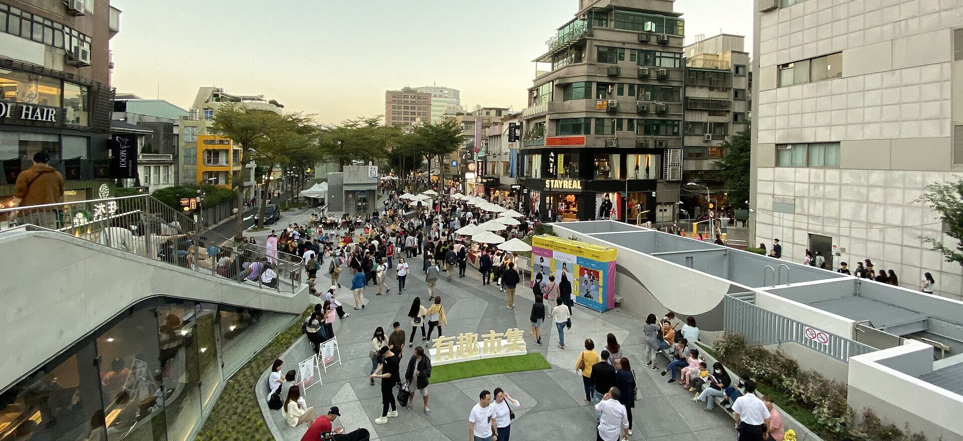 Visitors walk and sit beside shops and market umbrellas in Taipei's Zhongshan Shuanglian Linear Park.